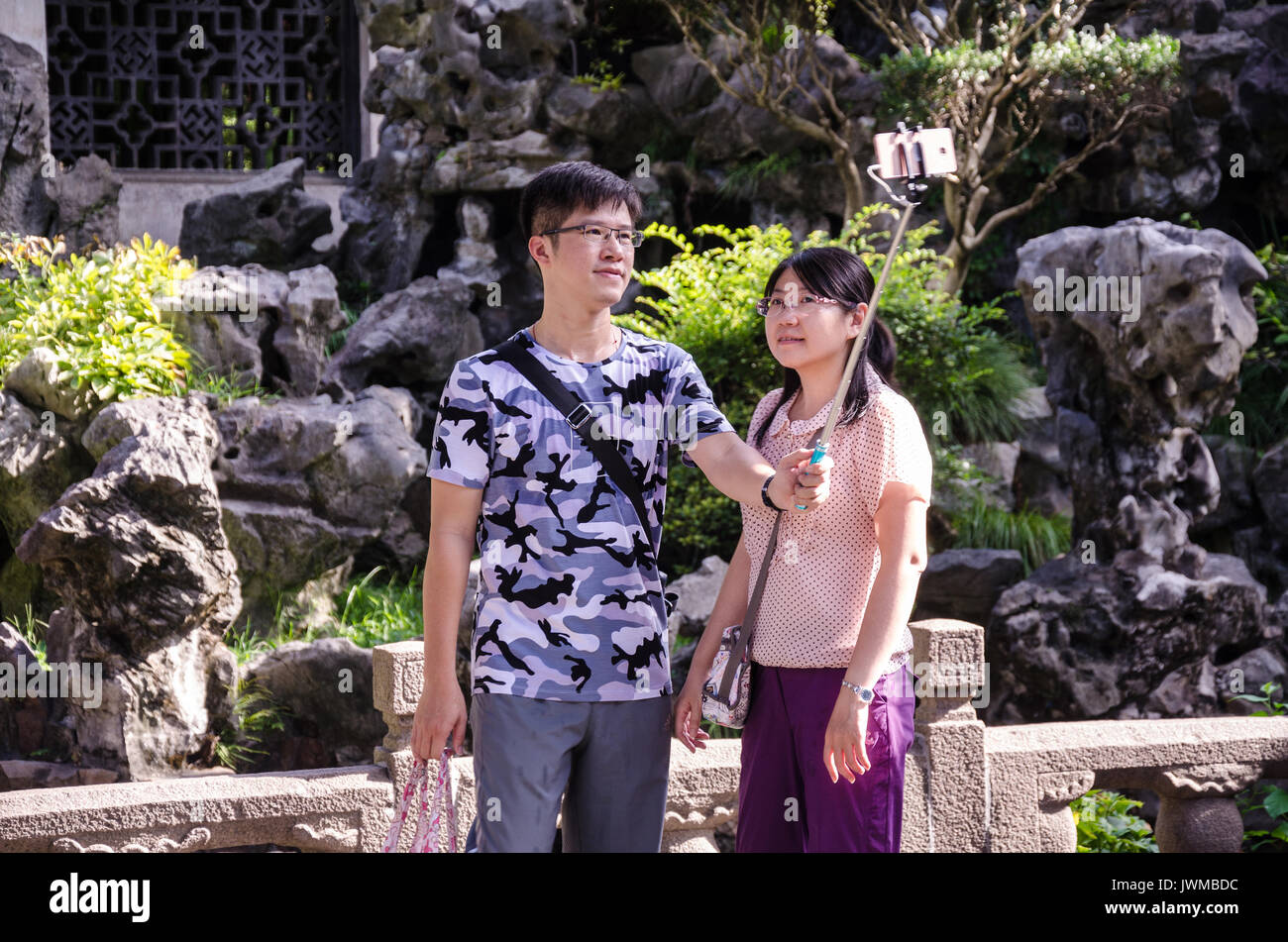 A young Chinese couple stop and take selfies using a smartphone on a selfie stick in Yuyuan Gardens in Shanghai, China. Stock Photo