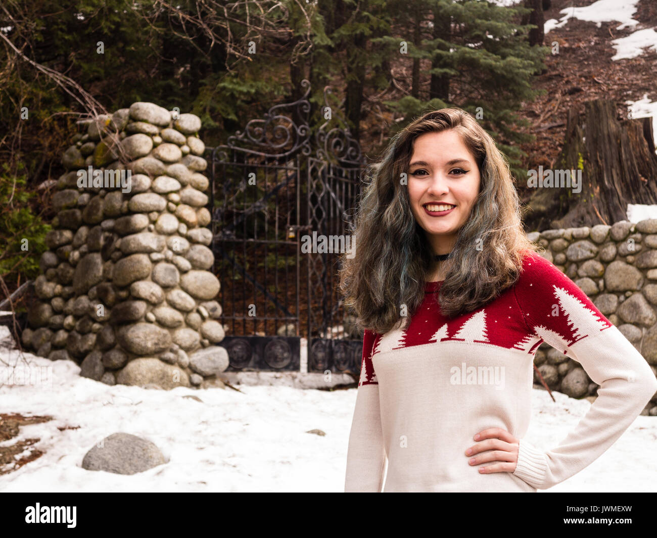 A smiling teen girl in red and white sweater by an iron gate with stone gateposts in winter Stock Photo