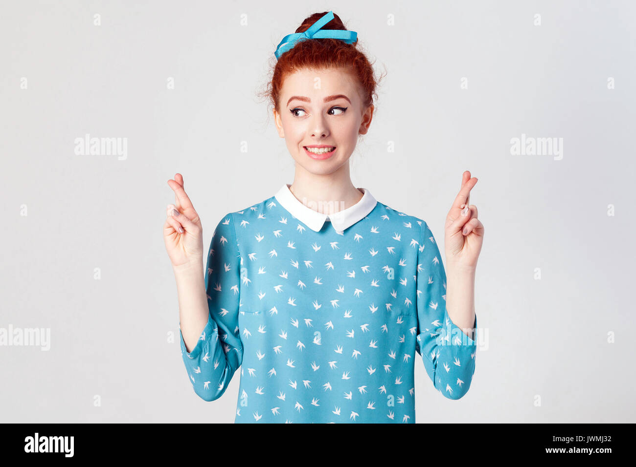 Body language. Human emotions and feelings. Superstitious teenager girl with ginger hair and pretty face crossing fingers for good luck, hoping her wi Stock Photo