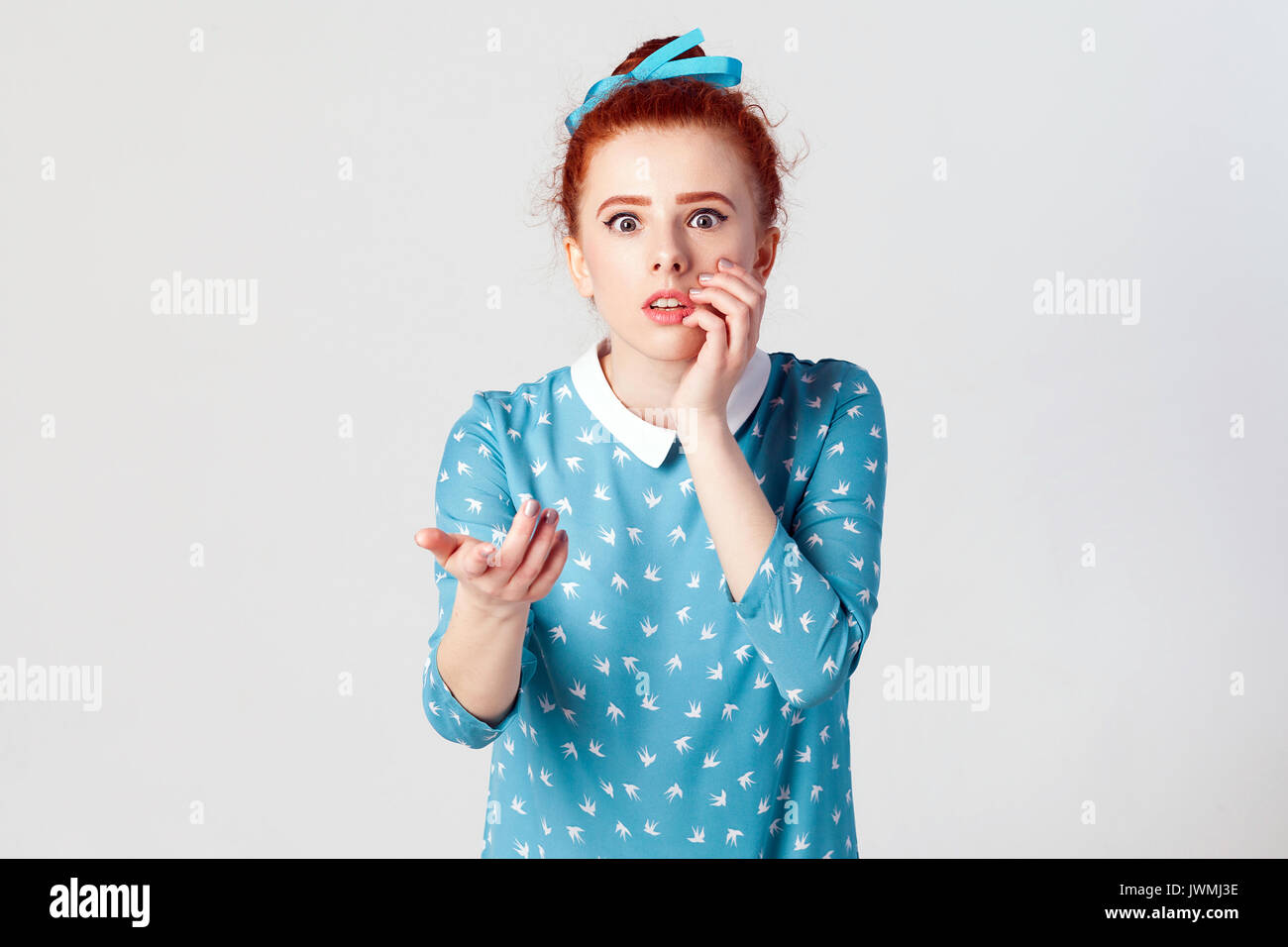 Human facial expressions, emotions and feelings. Beautiful redhead girl with hair knot having scared and frightened look, keeping mouth open, touching Stock Photo
