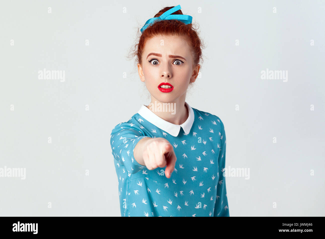 The beautiful caucasian girl, wearing blue dress, opening mouths widely, having surprised shocked looks, pointing finger at camera. Selective focus. I Stock Photo