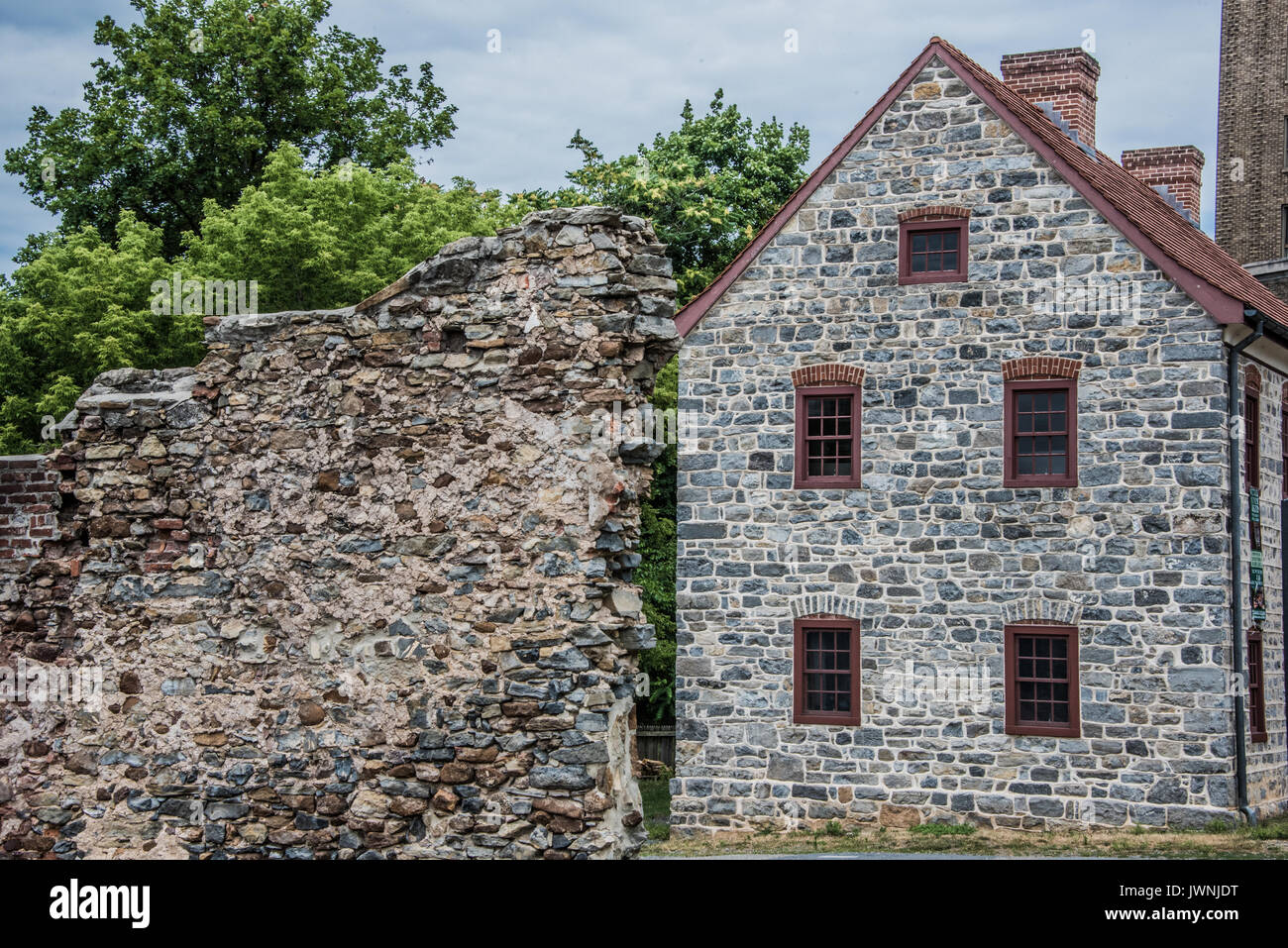 Old stone wall near colonial house during summer. Green trees and dark ...