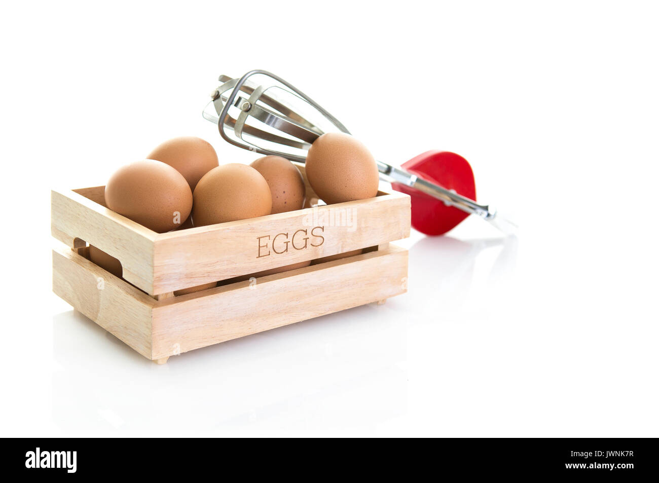 Eggs in a wooden box with old red egg whisk on a white background Stock Photo