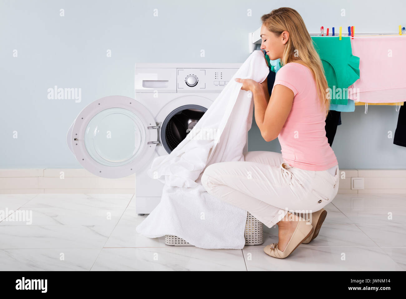 Woman Smelling Cleaned Clothes Near The Electronic Washer At Laundry Room Stock Photo