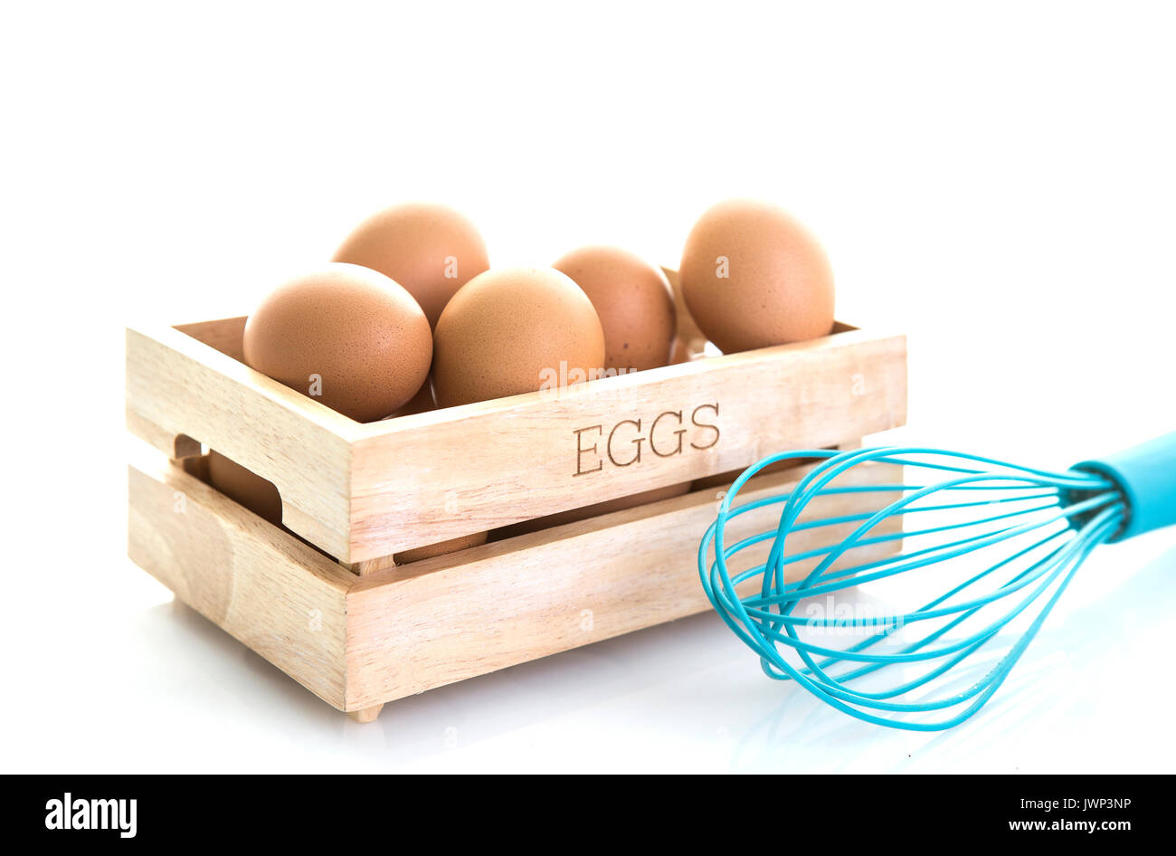 Eggs in a wooden box with blue egg whisk on a white background Stock Photo