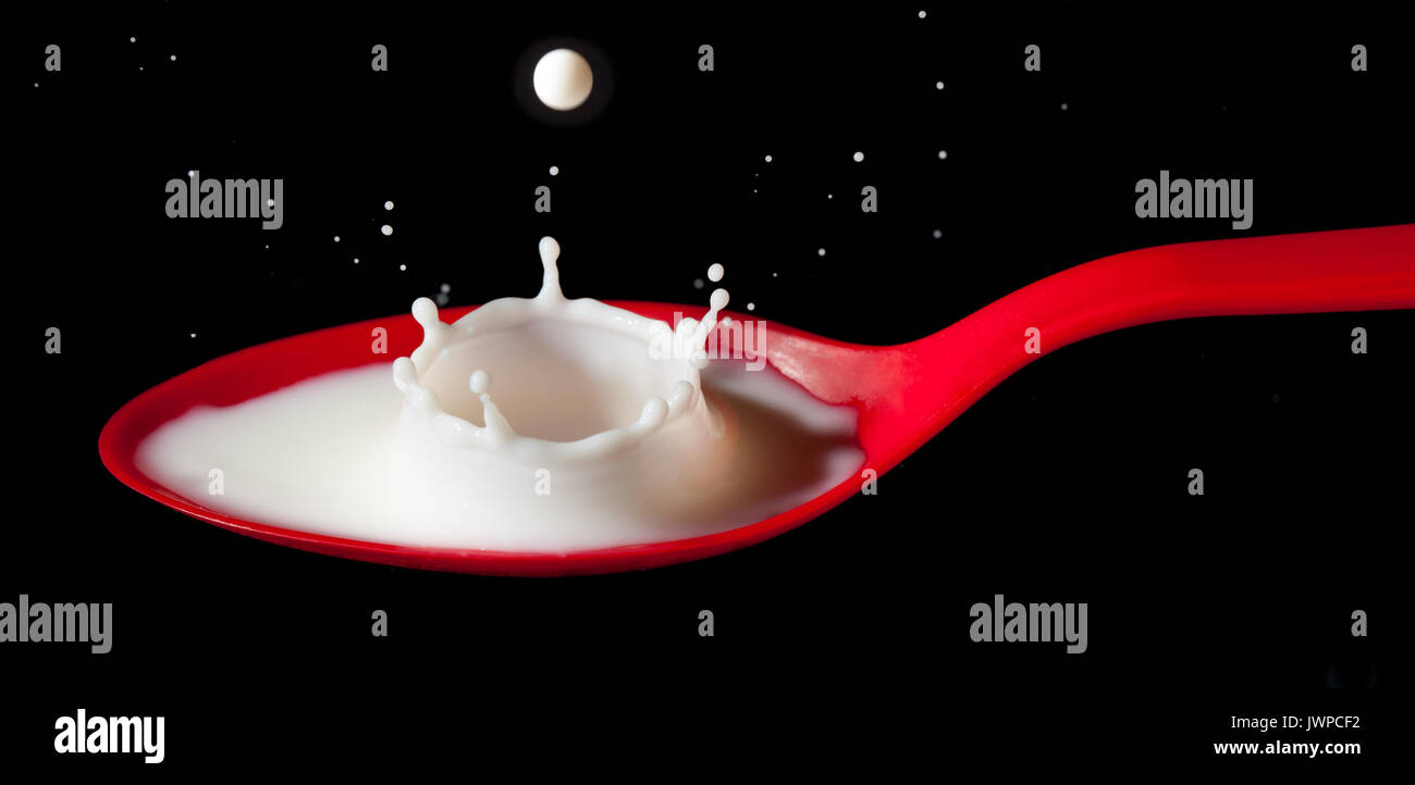 White milk splashing into red spoon Stock Photo