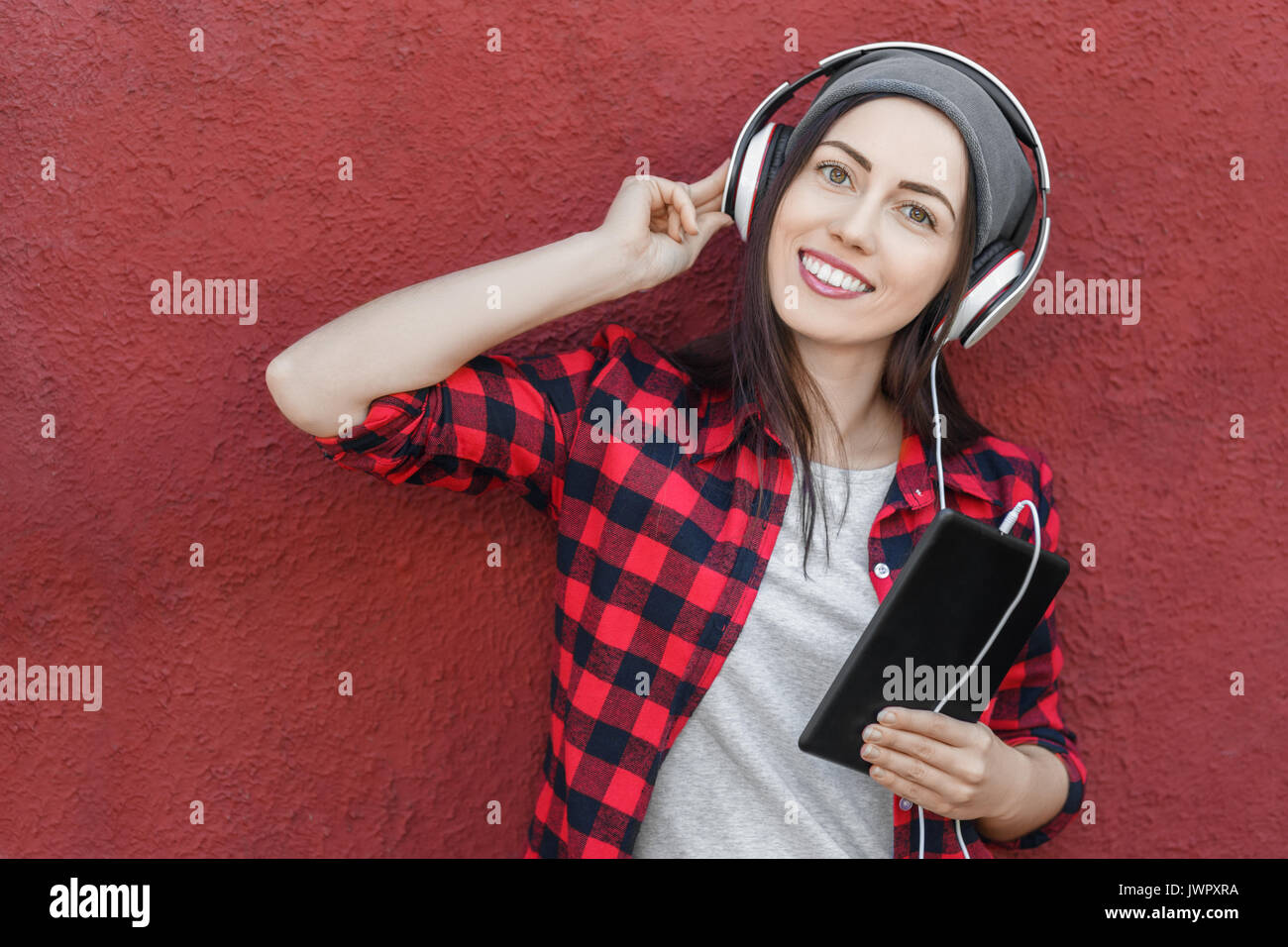 young woman with tablet computer listening music in headphones. Girl using digital tablet outdoors. Copy space. Technology, music, lifestyle, and mill Stock Photo