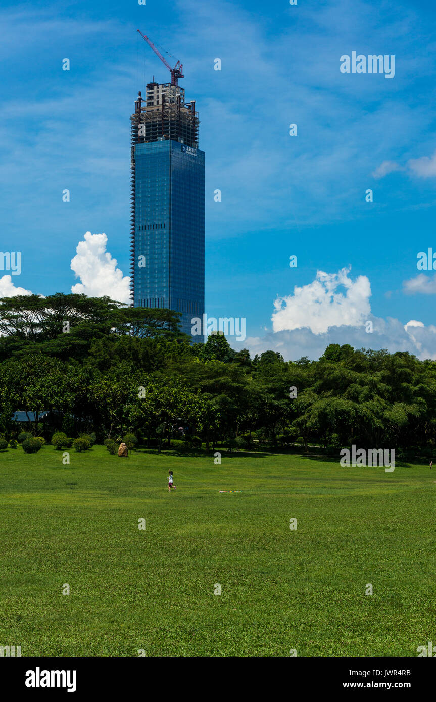 Unfinished office tower in Shenzhen, China, overlooking a park as young child tries to fly a kite Stock Photo