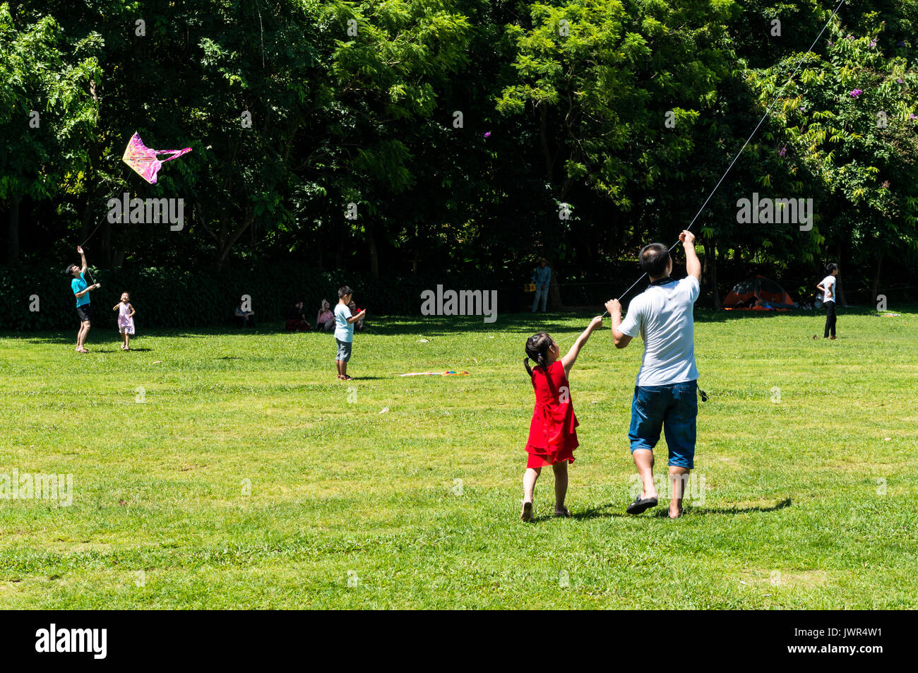 Father and daughter, likely middle class Chinese, fly a kite together at Lianhuashan Park on a sunny afternoon in Shenzhen, China Stock Photo