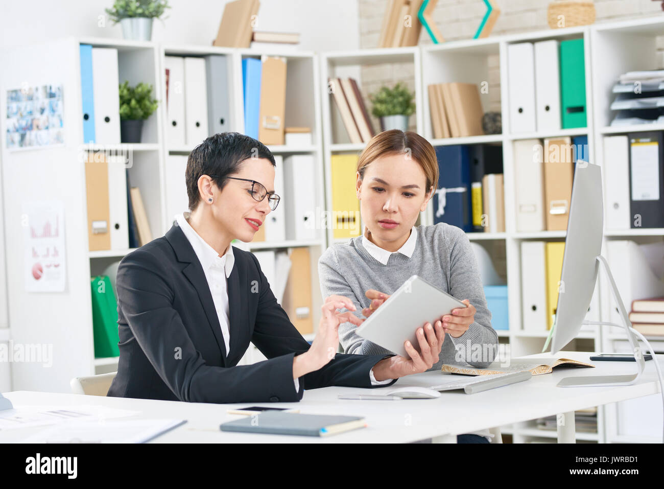 Concentrated managers analyzing results of accomplished work while having working meeting in modern office, they using digital tablet Stock Photo