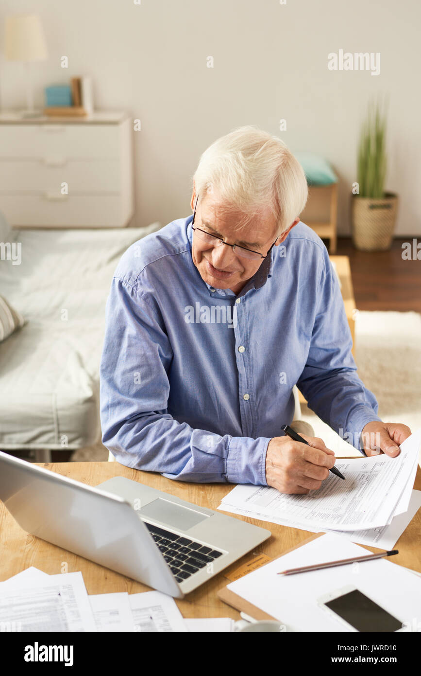 Portrait of modern senior man filling in application while working with laptop at home in cozy living room Stock Photo