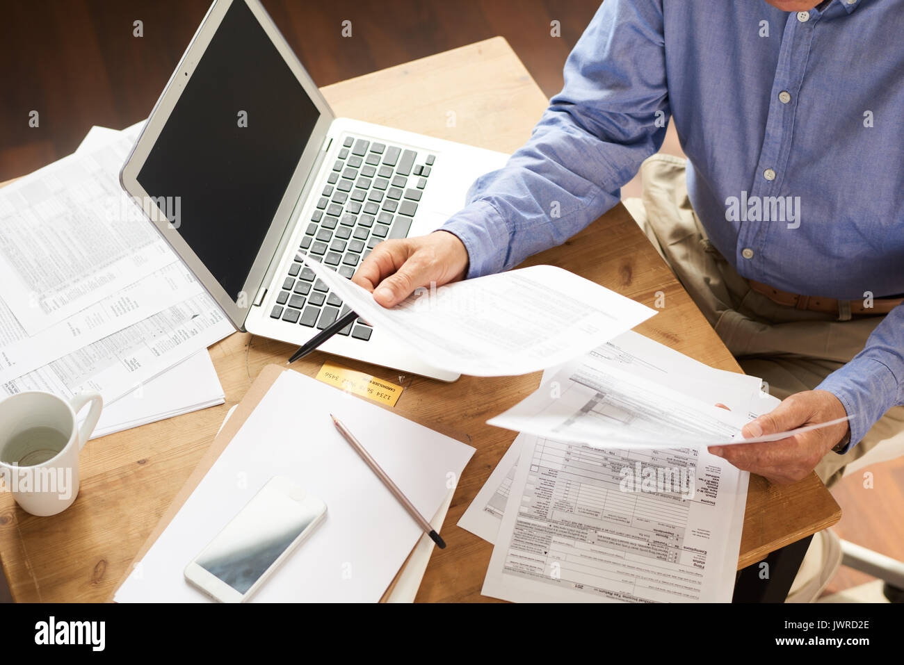 Closeup of unrecognizable senior man filling in application papers at home sitting at table with laptop Stock Photo