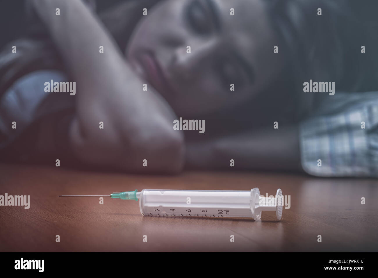 Close-up of a syringe with drugs beside lies a young woman. Focus on the syringe Stock Photo