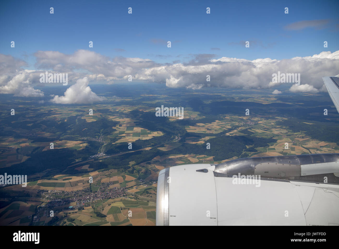 Patchwork of green, orange and yellow fields as well as woodland and villages as seen from plane over Central Europe.  Part of the engine is visible i Stock Photo