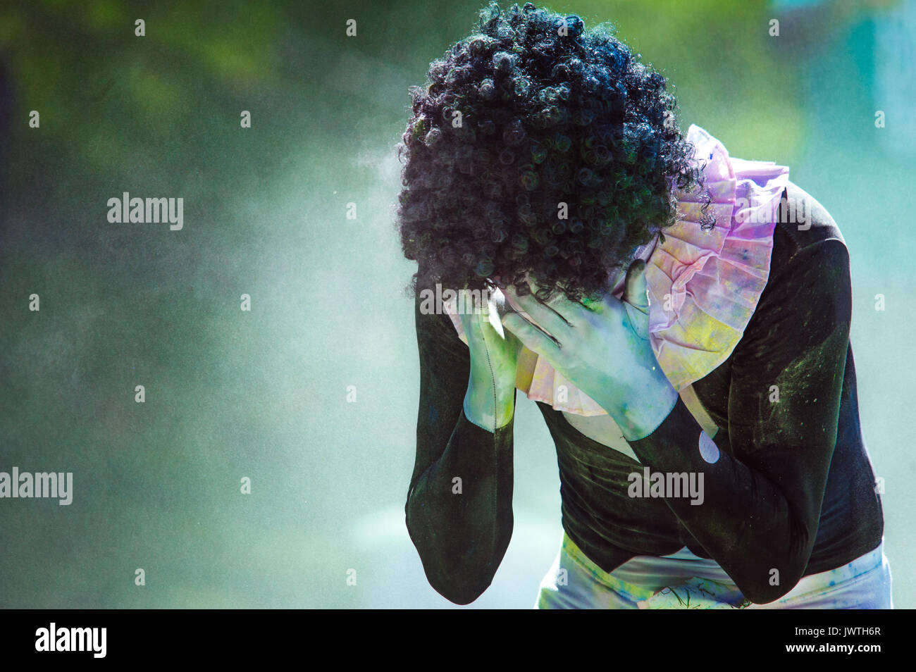 Crying clown in a body suit and afro wig covered in paint at a Color Run Stock Photo