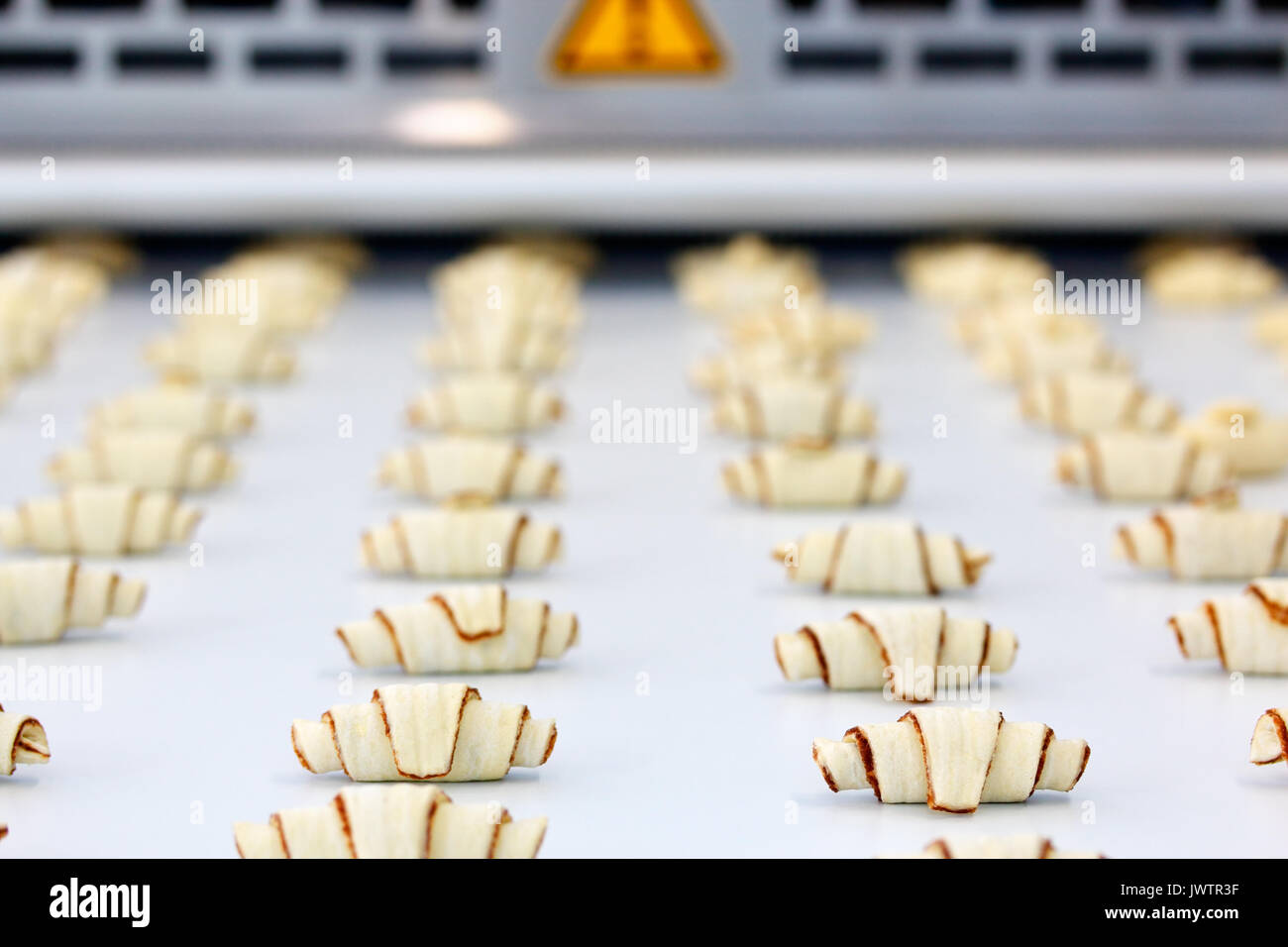 The process of producing croissants on an automatic industrial machine line. Selective focus. Stock Photo