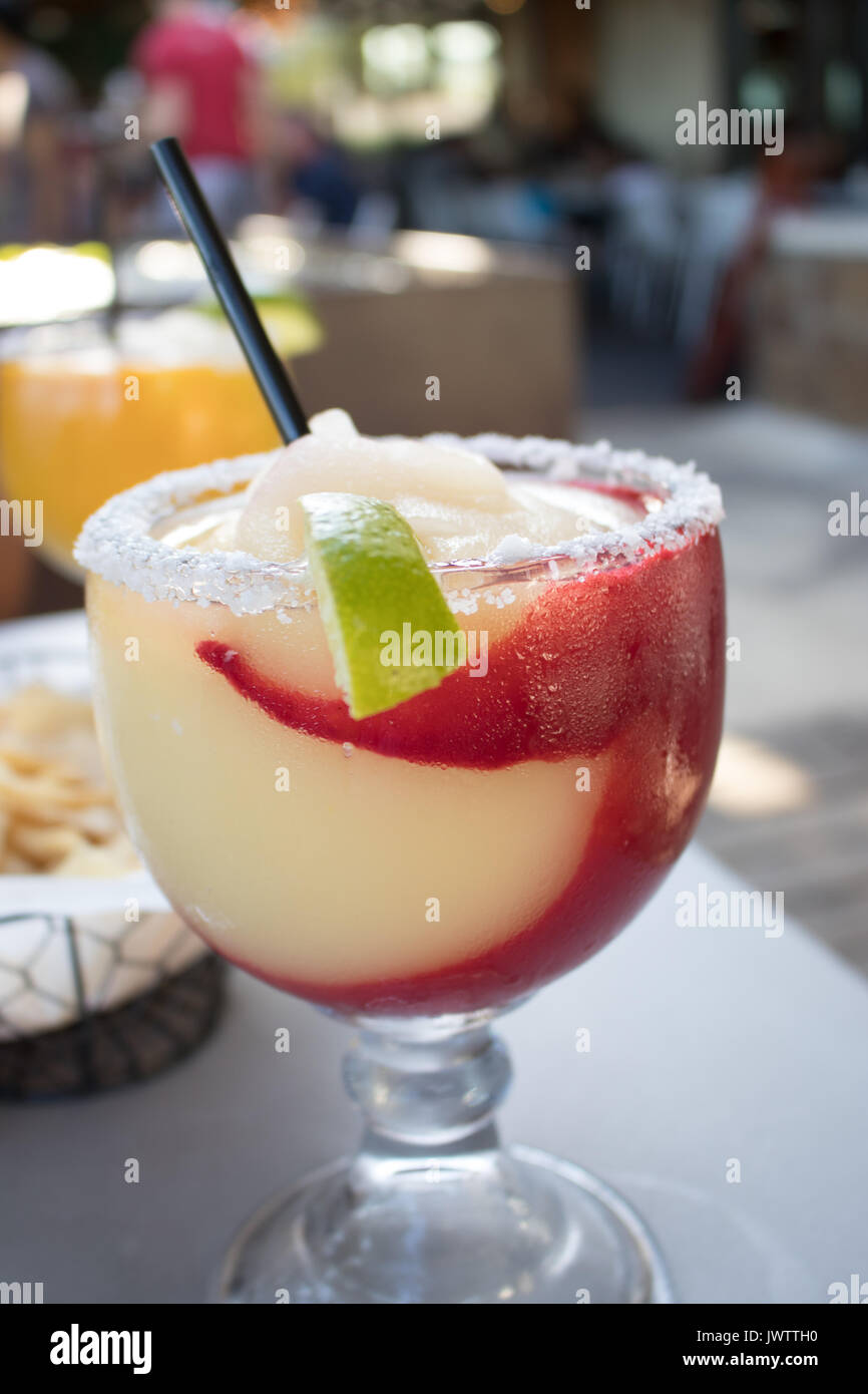 Large goblet frozen margarita with raspberry swirl, salted rim and lime slice. blurred restaurant in the background. Stock Photo