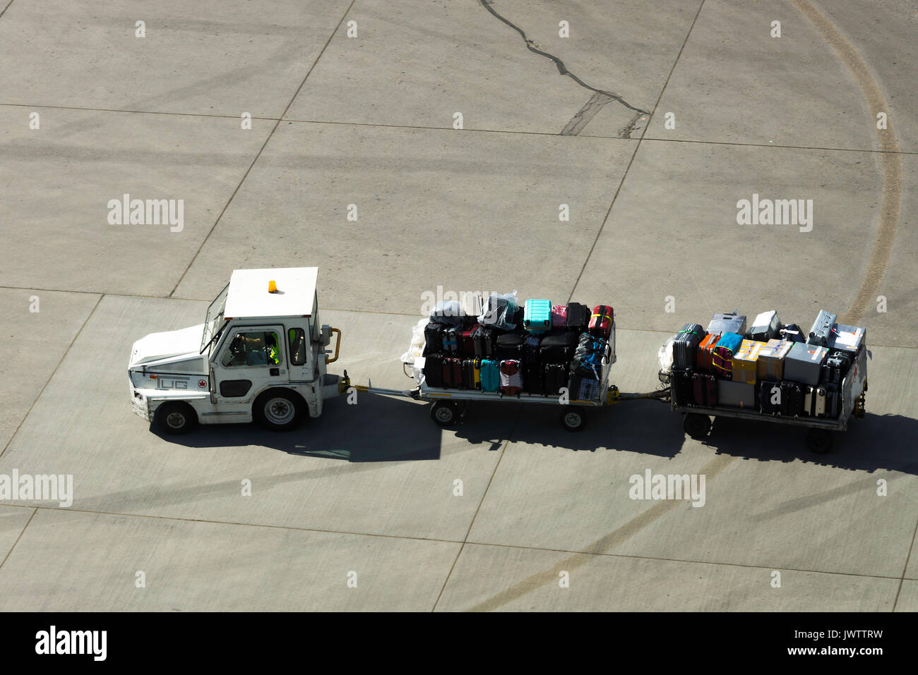 Suitcases on Trolleys Being Pulled by a Tug on Roadway Prior to Loading on Aircraft at Calgary International Airport Alberta Canada Stock Photo