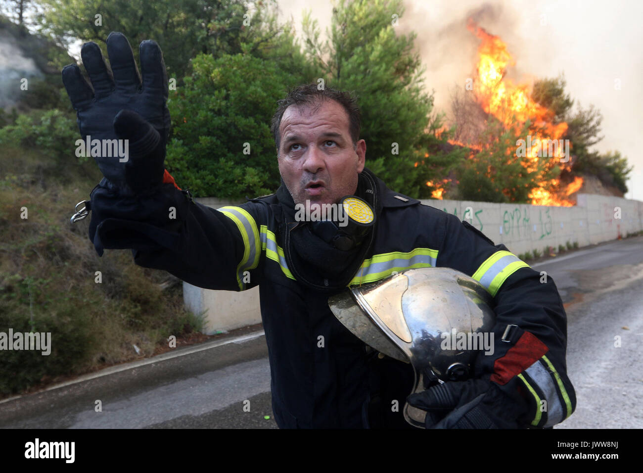 Kalamos Village, Greece. 13th Aug, 2017. A firefighter signals an helicopter during a forest fire. Credit: SOPA Images Limited/Alamy Live News Stock Photo
