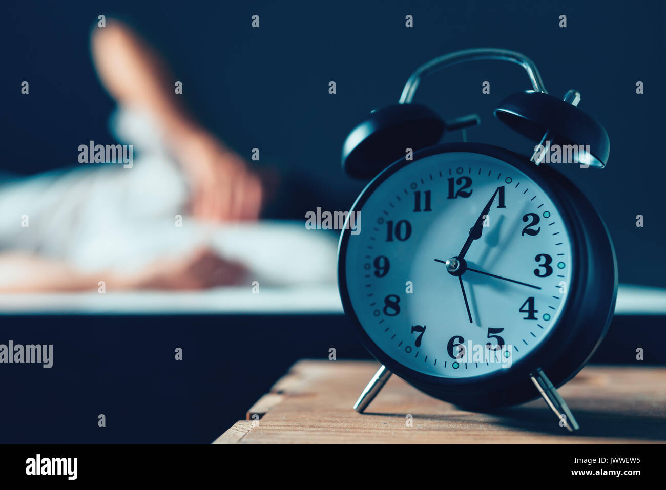 Sleeping disorder or insomnia concept, selective focus of vintage clock in bedroom and out of focus male person trying to fall asleep in bed Stock Photo