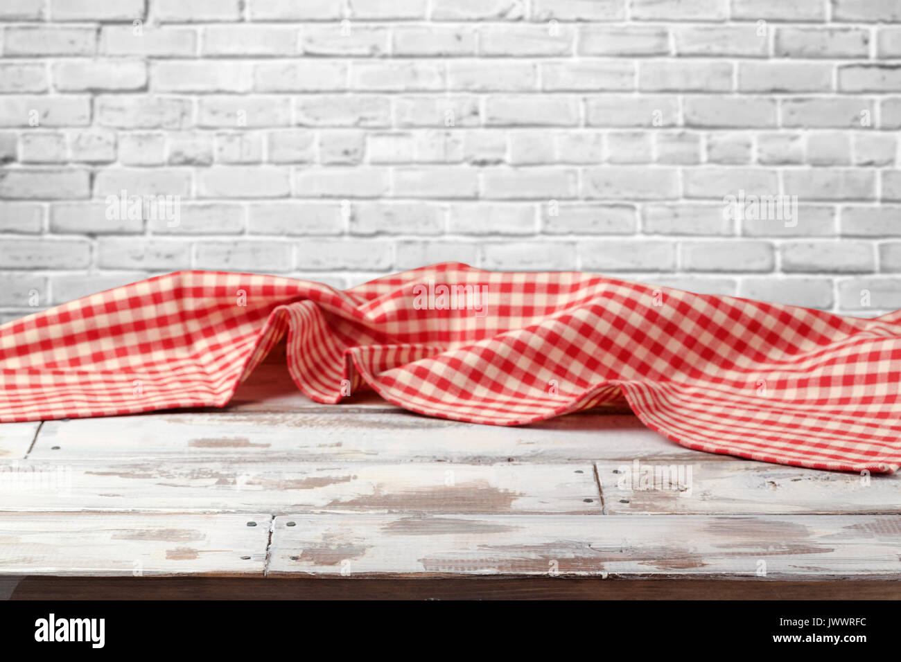 Empty wooden table with red checked tablecloth over brick wall background Stock Photo