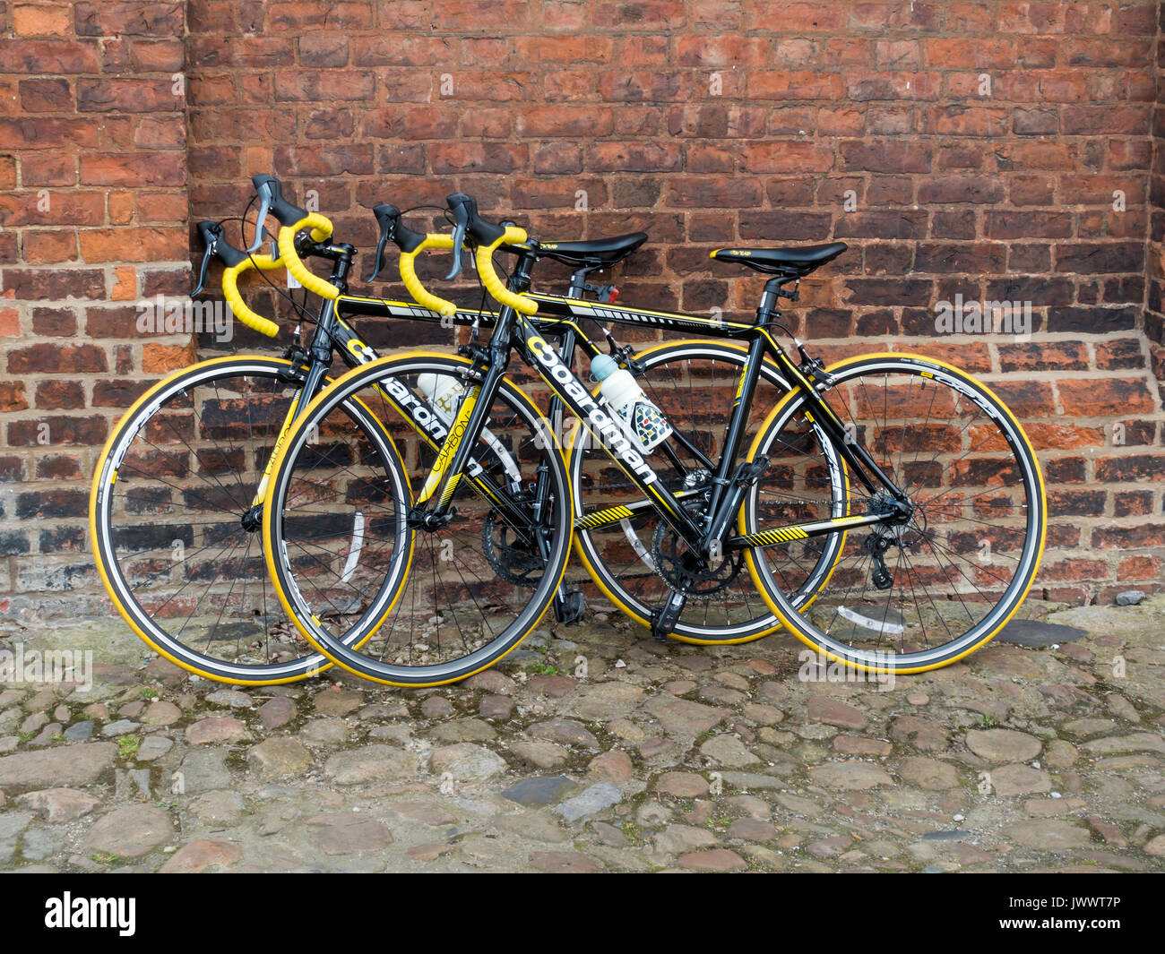 Two high quality black and yellow sports bicycles Boardman brand, parked against a brick wall while the riders are in a nearby café. Stock Photo