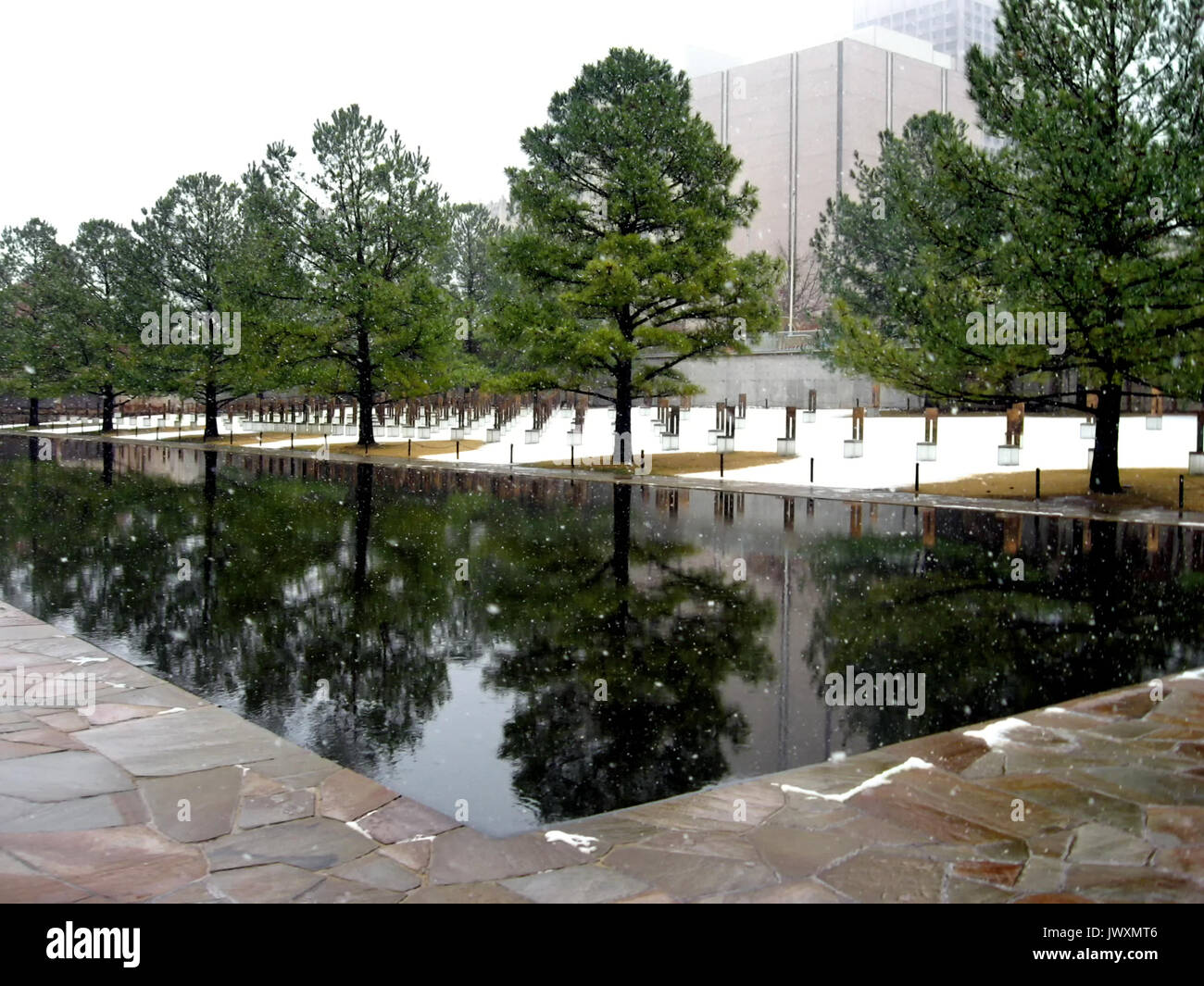 The Reflecting Pool at the Oklahoma City National Memorial mirrors the beautiful evergreens, the memorial chairs, and the falling snow in winter. Stock Photo