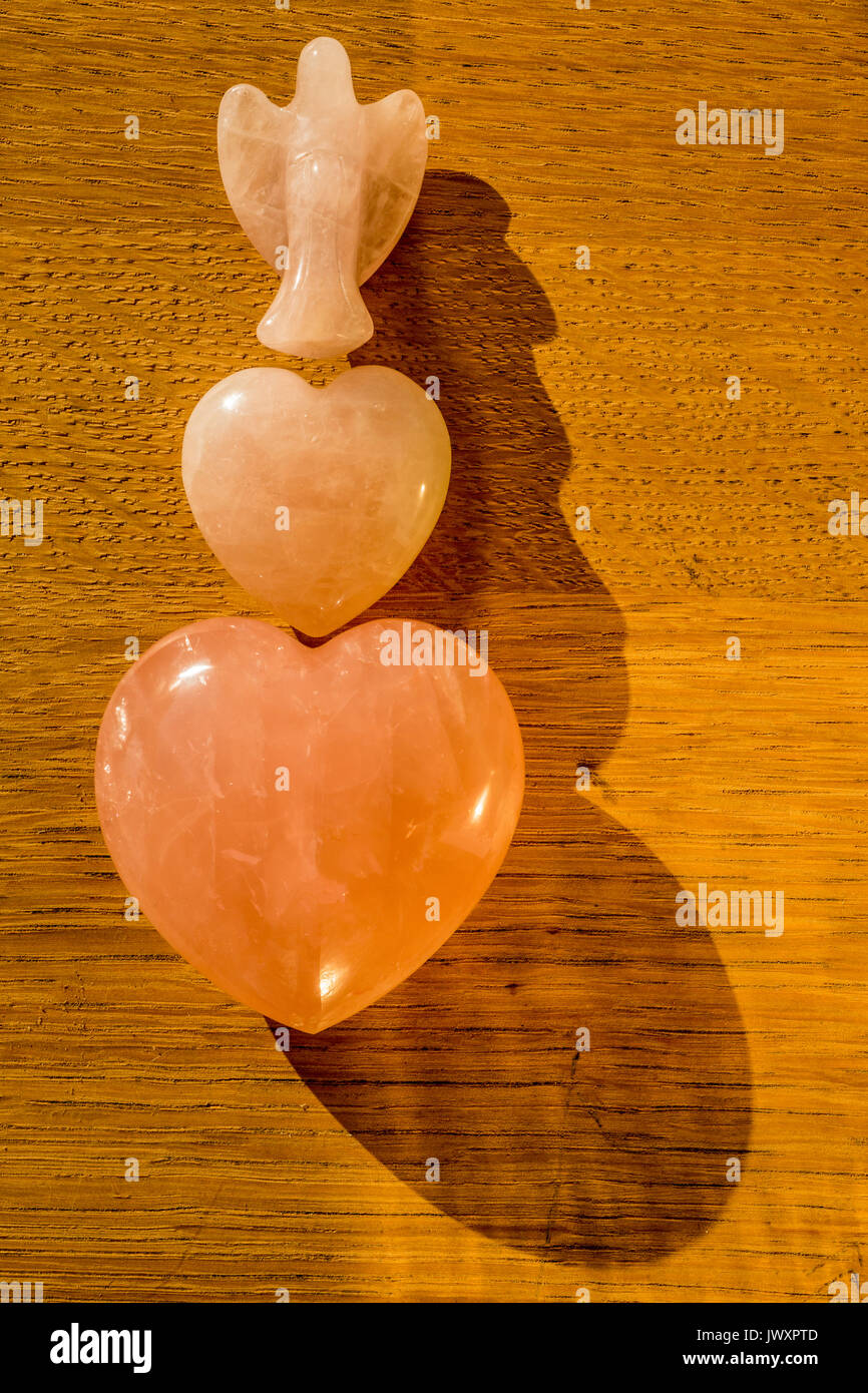 2 X Rose quartz heart shaped and 1 X Angel shaped flat lay on natural wood. Stock Photo