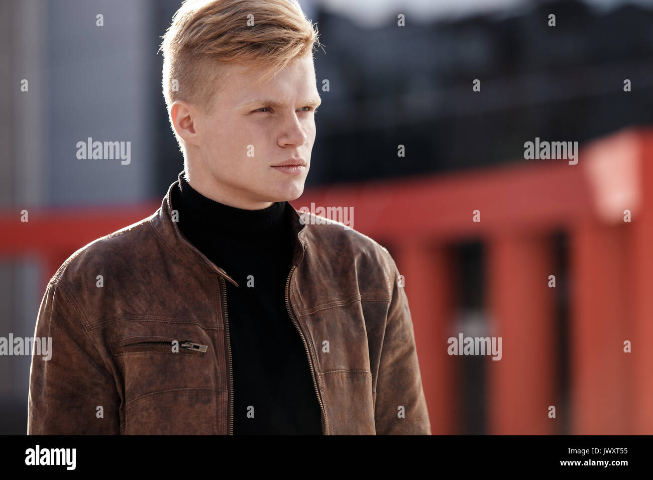 Young stylish man in brown jacket is looking away while standing outdoors. Street style Stock Photo