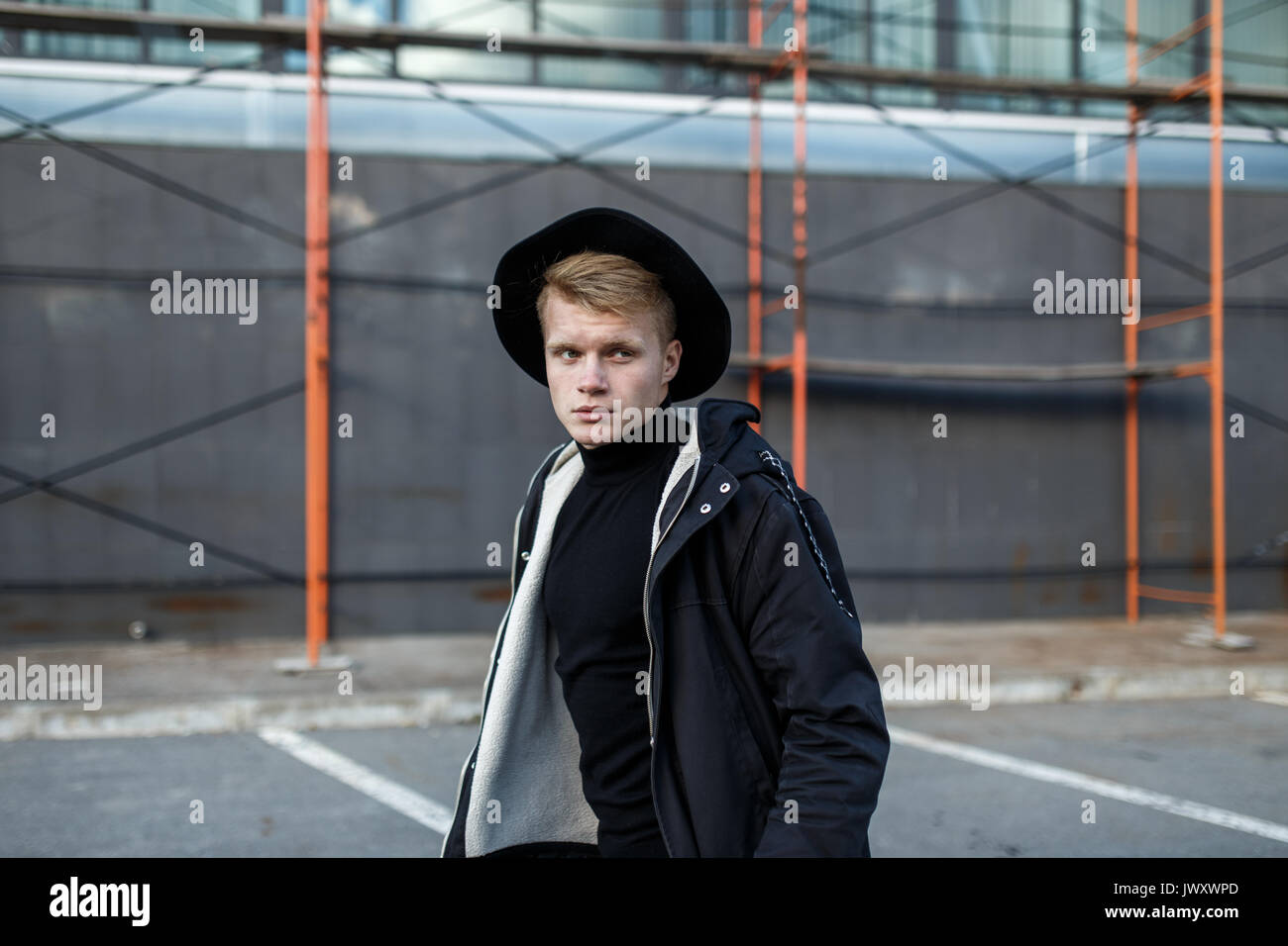 Young stylish man in trendy wear is looking away while standing outdoors. Street style. Stock Photo
