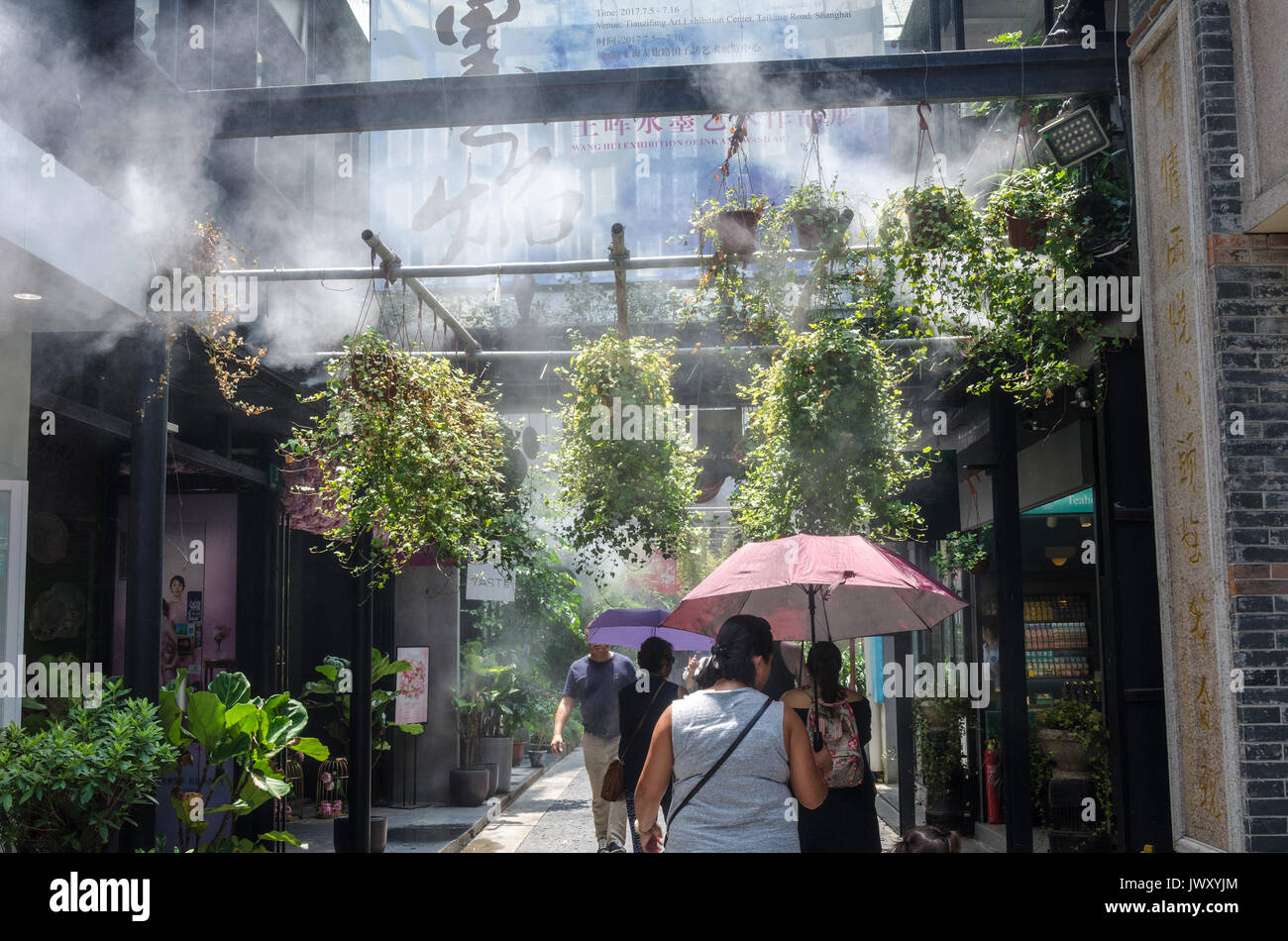 Tourists wander the streets of Tianzifang in Shanghai, China. A cooling system sprays a mist to bring relief from the hot sun. Stock Photo