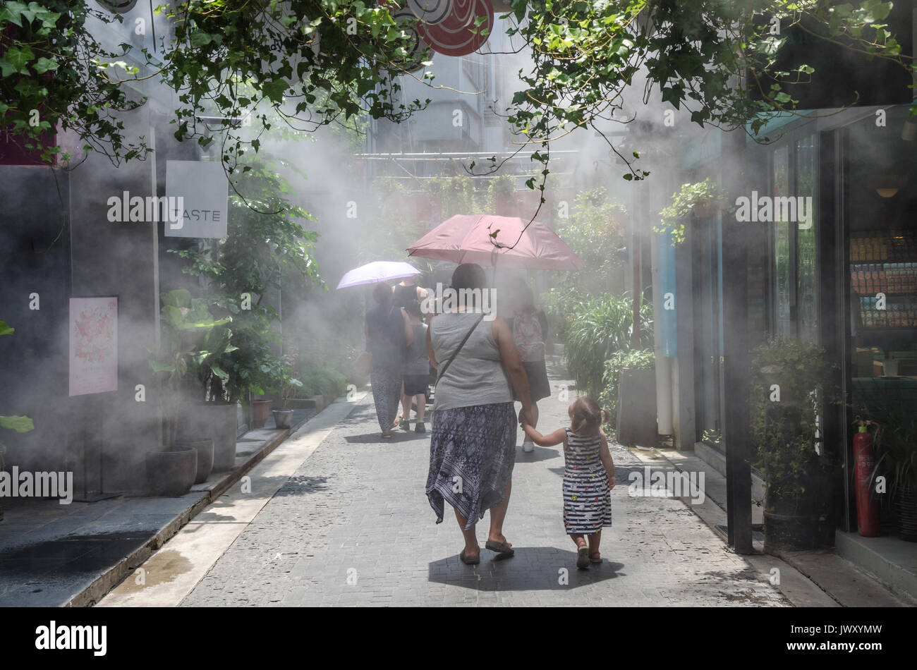 A mother and child walk around the streets of Tianzifang in Shanghai, China. Mist is sprayed from a cooling system to bring relief form the hot sun. Stock Photo