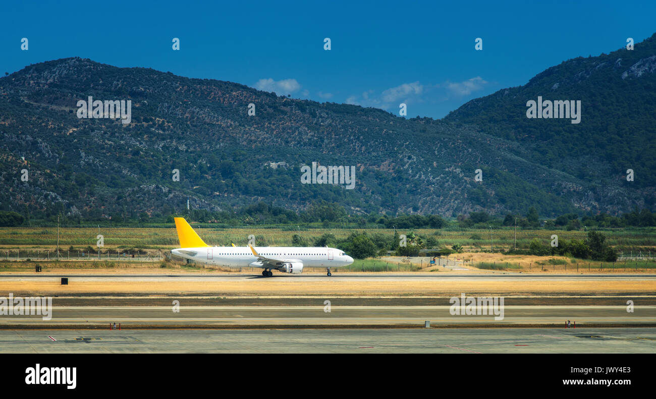 Beautiful white airplane on the runway in Dalaman airport. Landscape with big passenger airplane is taking off and mountains at bright sunny day Stock Photo