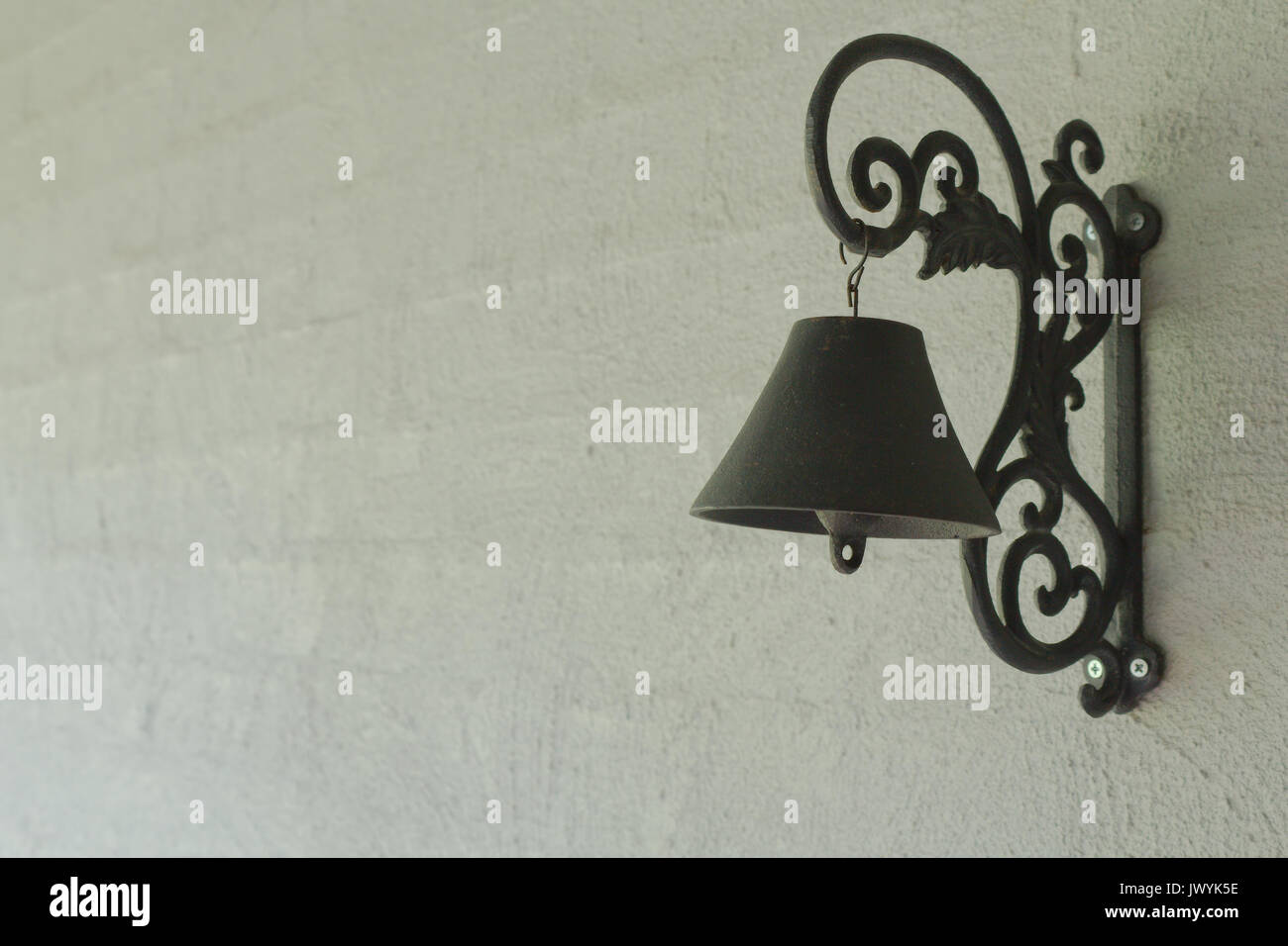 A black iron door bell hanging on a grey rendered brick wall in the entrance way to a home. Stock Photo