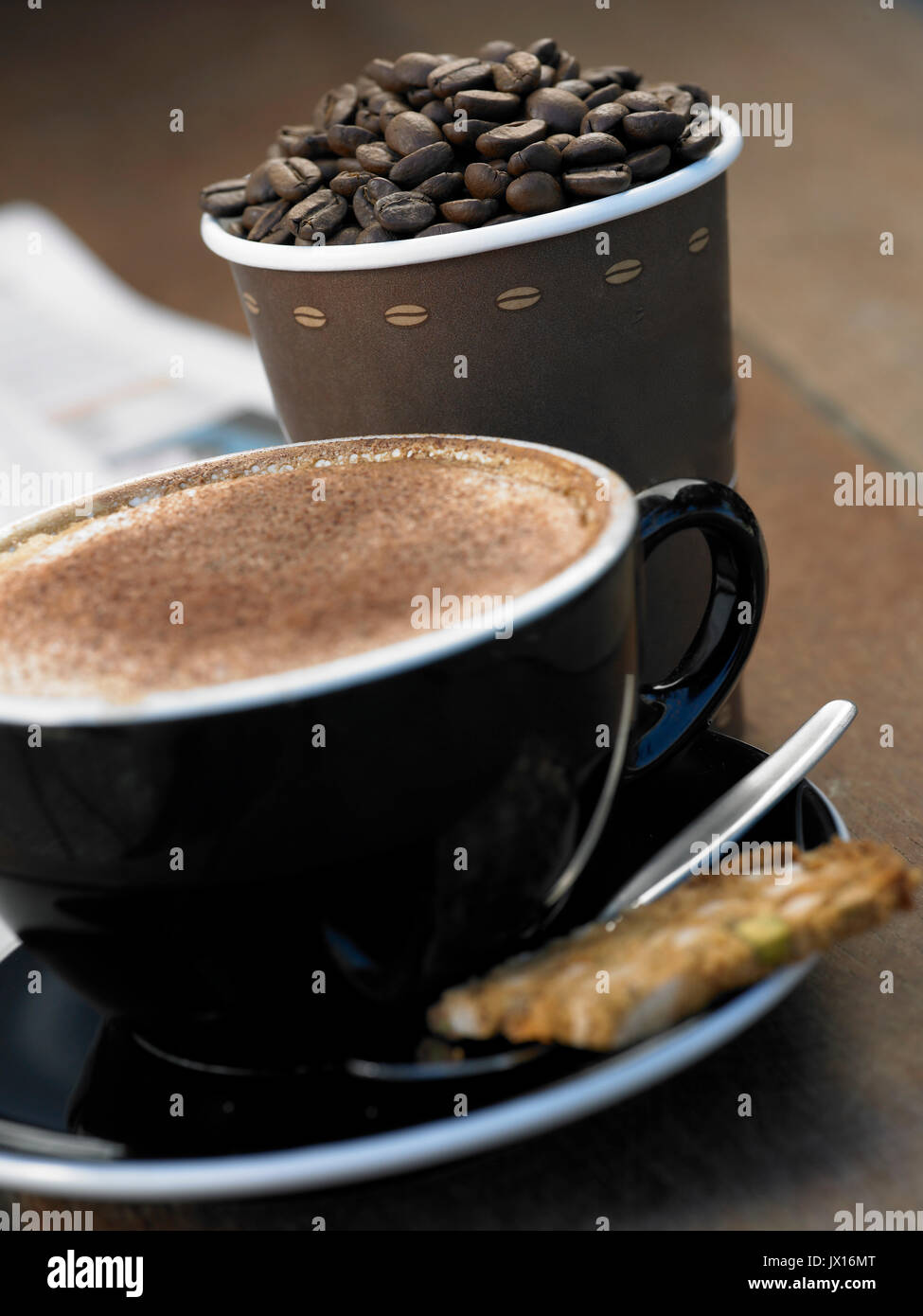 cappuccino coffee with cinnamon with takeaway cup full of beans ,newspaper and biscotti Stock Photo