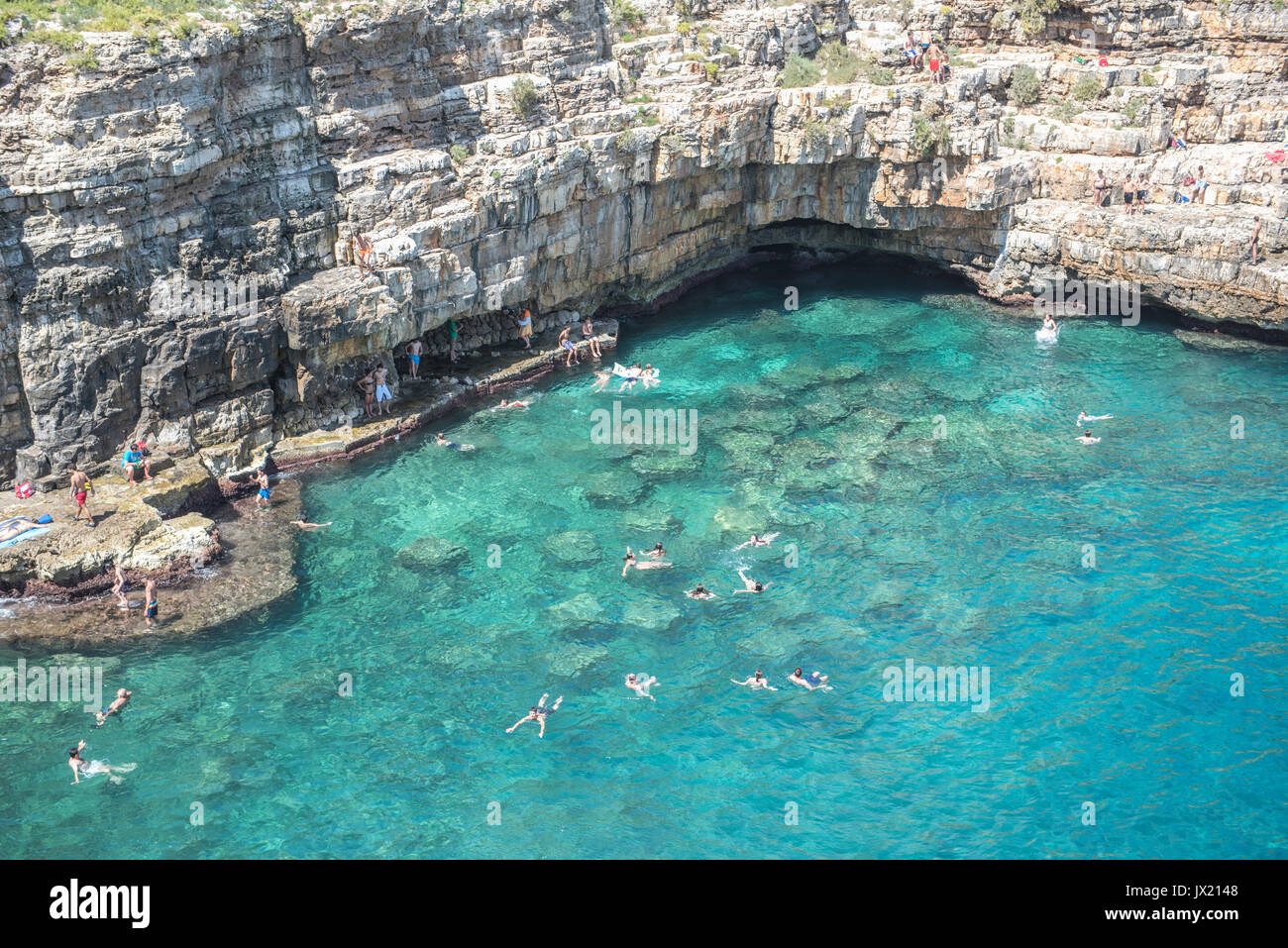 Swimmers wade into the spectacular turquoise ocean at Polignano A Mare. The beach is also the site of the annual Red Bull cliff-diving competition. Stock Photo