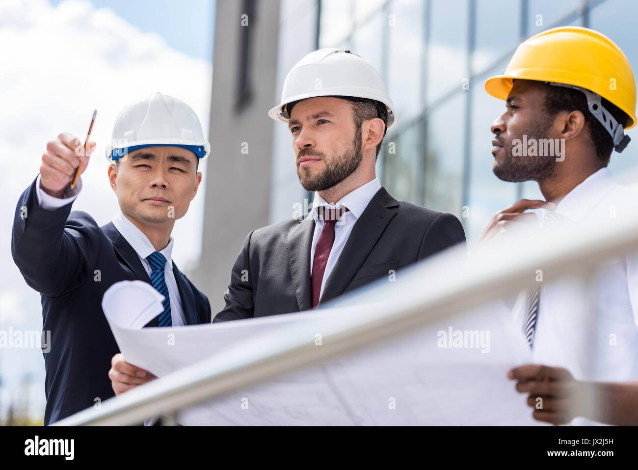 Professional architects in hardhats working with blueprint outside ...