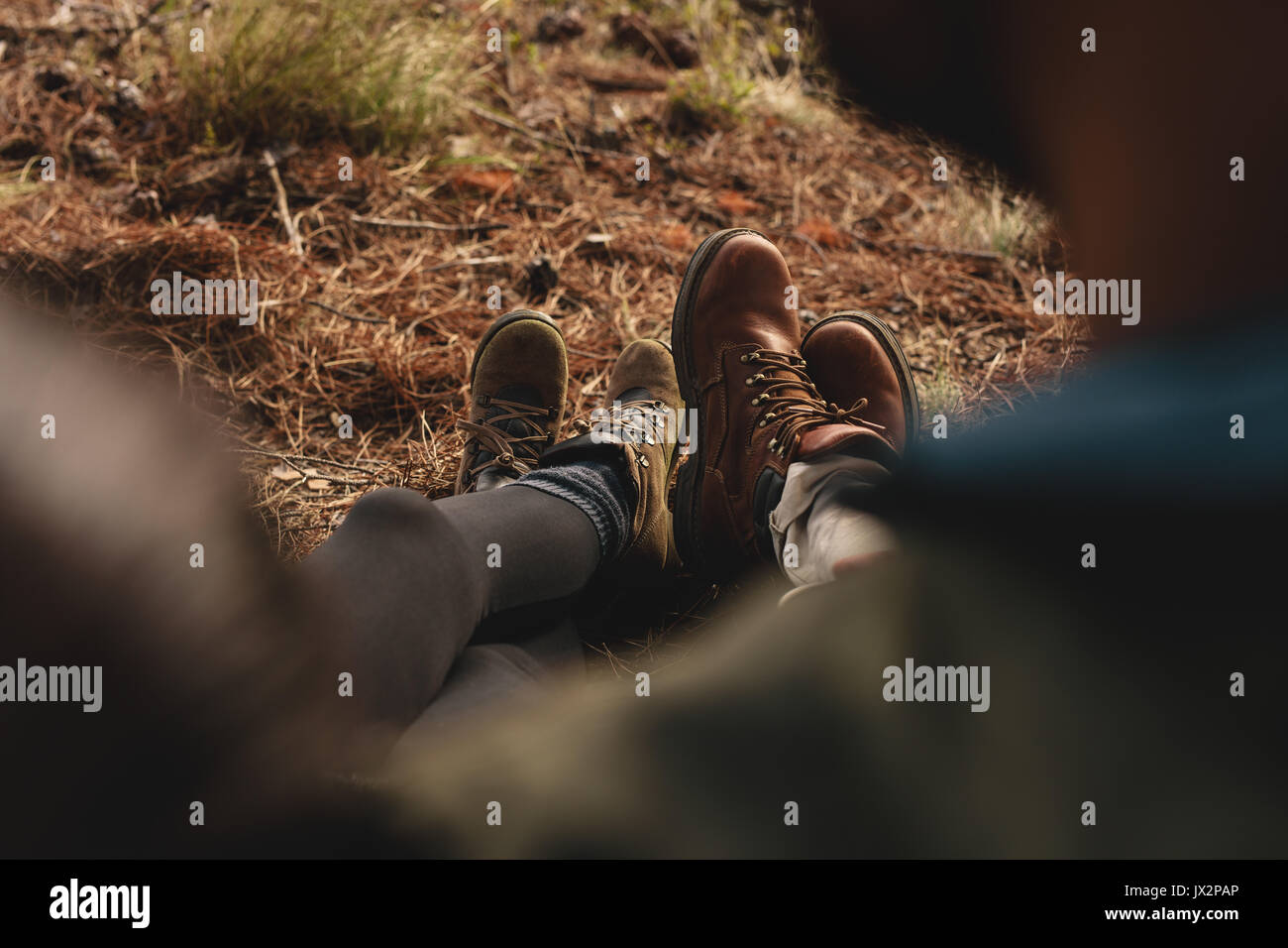 Close up of couple of hikers sitting together outdoors, focus on legs. Hikers resting on country trail. Stock Photo