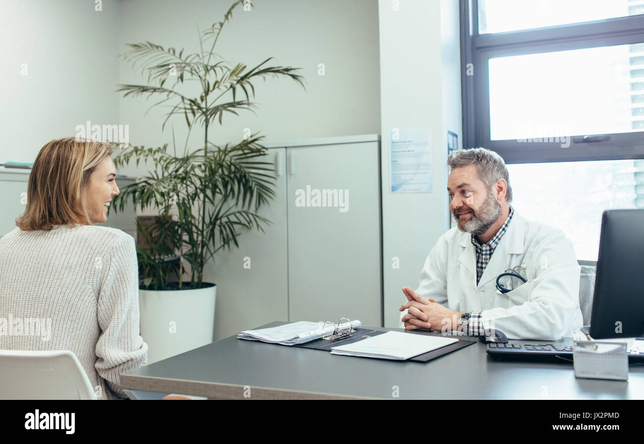 Happy medical doctor talking with woman sitting at office desk ...
