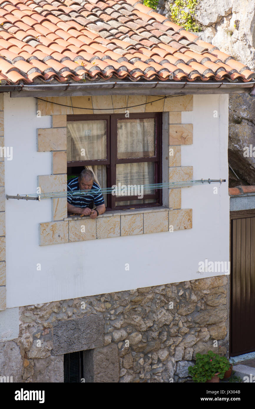 Older man leaning out of a window whilst breaking nuts in a town in northern Spain. Stock Photo