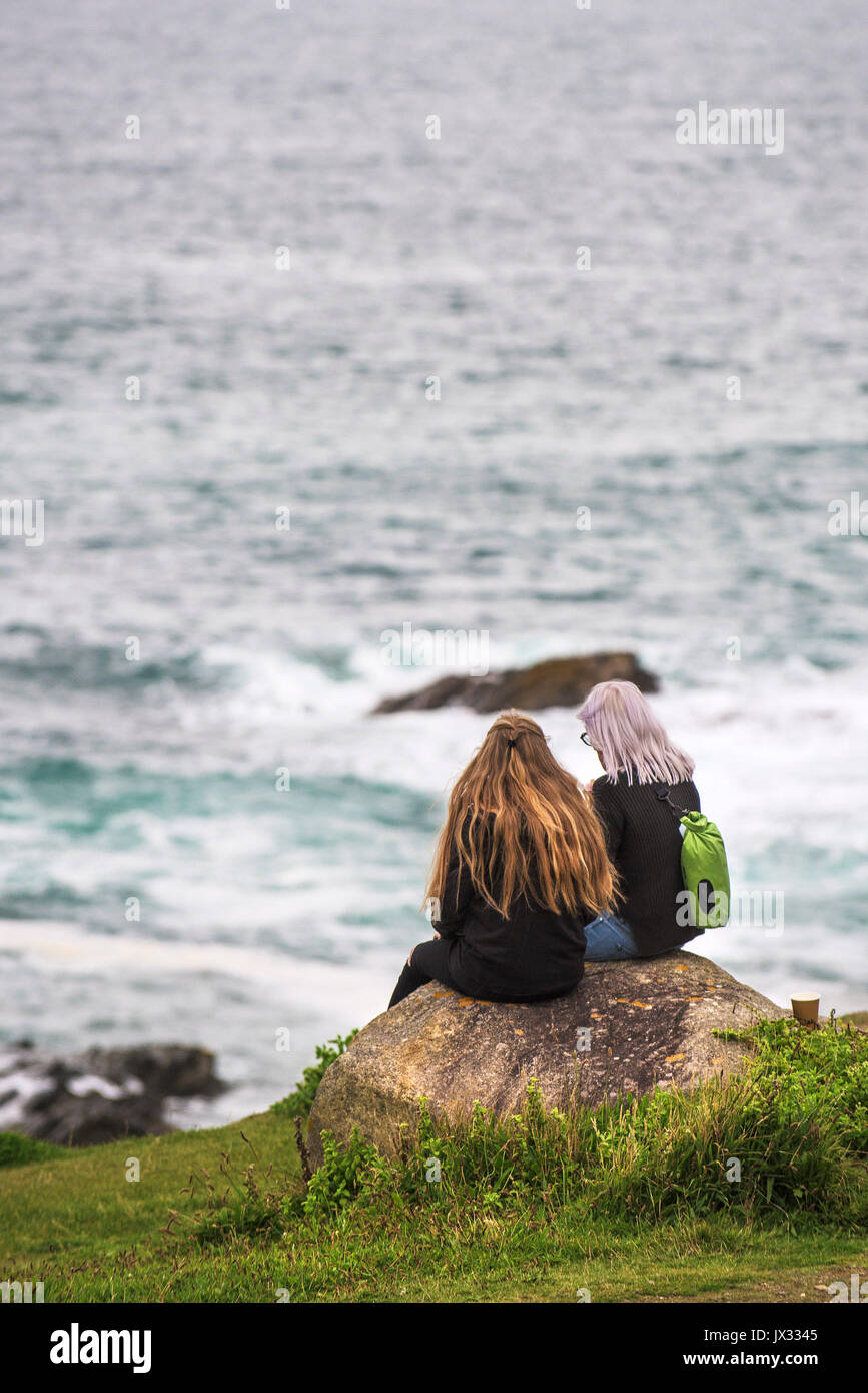 Two females sitting on a rock overlooking the sea. Stock Photo