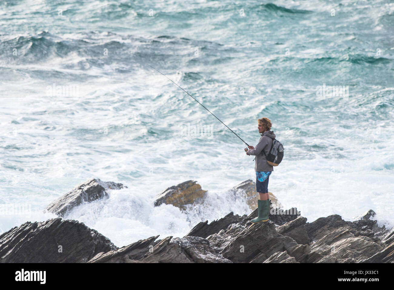 An angler fishing from rocks in Newquay, Cornwall. Stock Photo