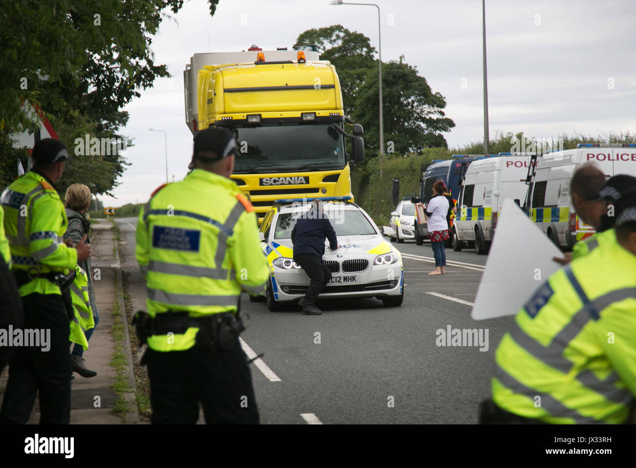 As a truck with equipment arrives at the Quadrilla fracking site a protester tries to stop the convoy by lying on top of  the leading police car. Stock Photo