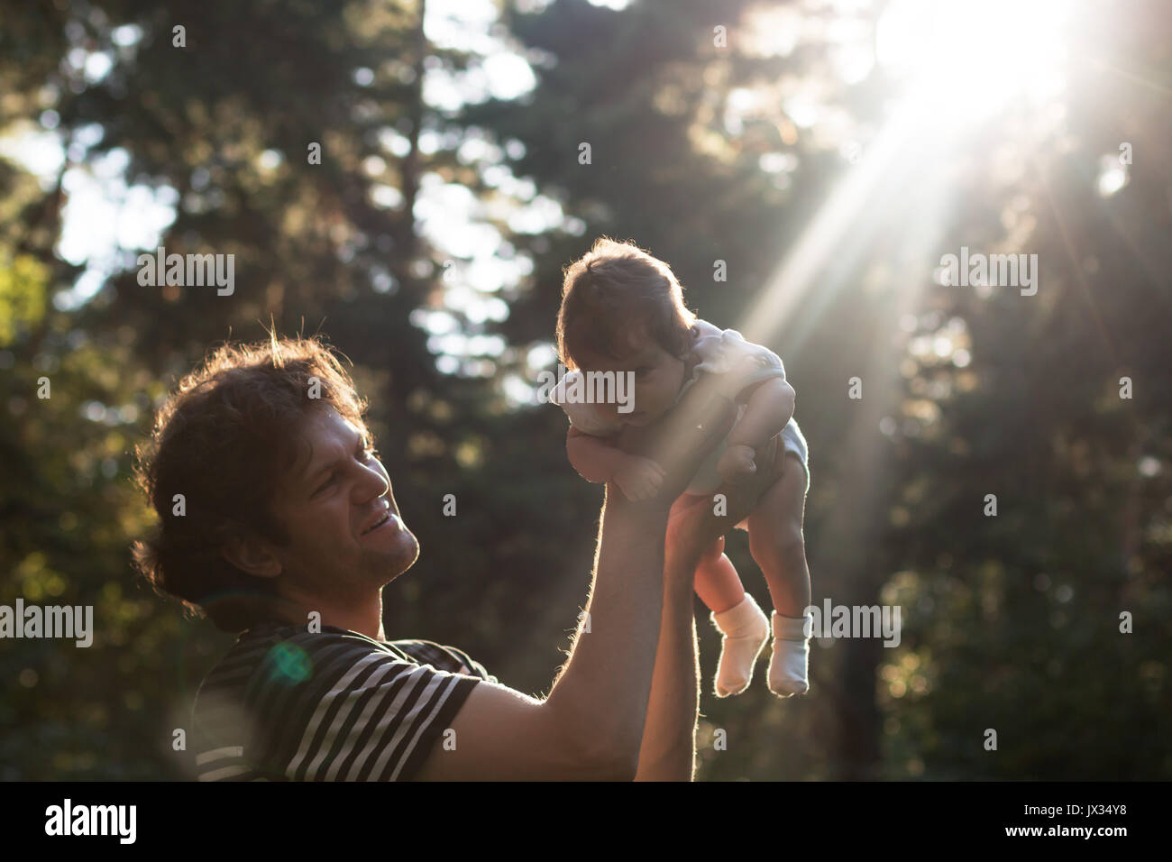 Happy joyful father having fun throws up in the air his child in the park in the evening - intentional sun glare and vintage color, lens focus on father. Father's day. Film filter Stock Photo