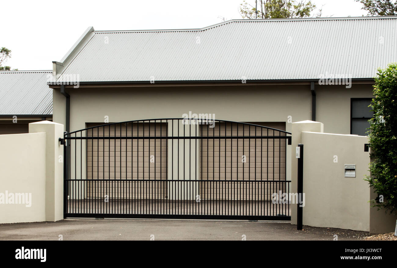 Metal driveway entrance gates set in brick fence with double car garage Stock Photo