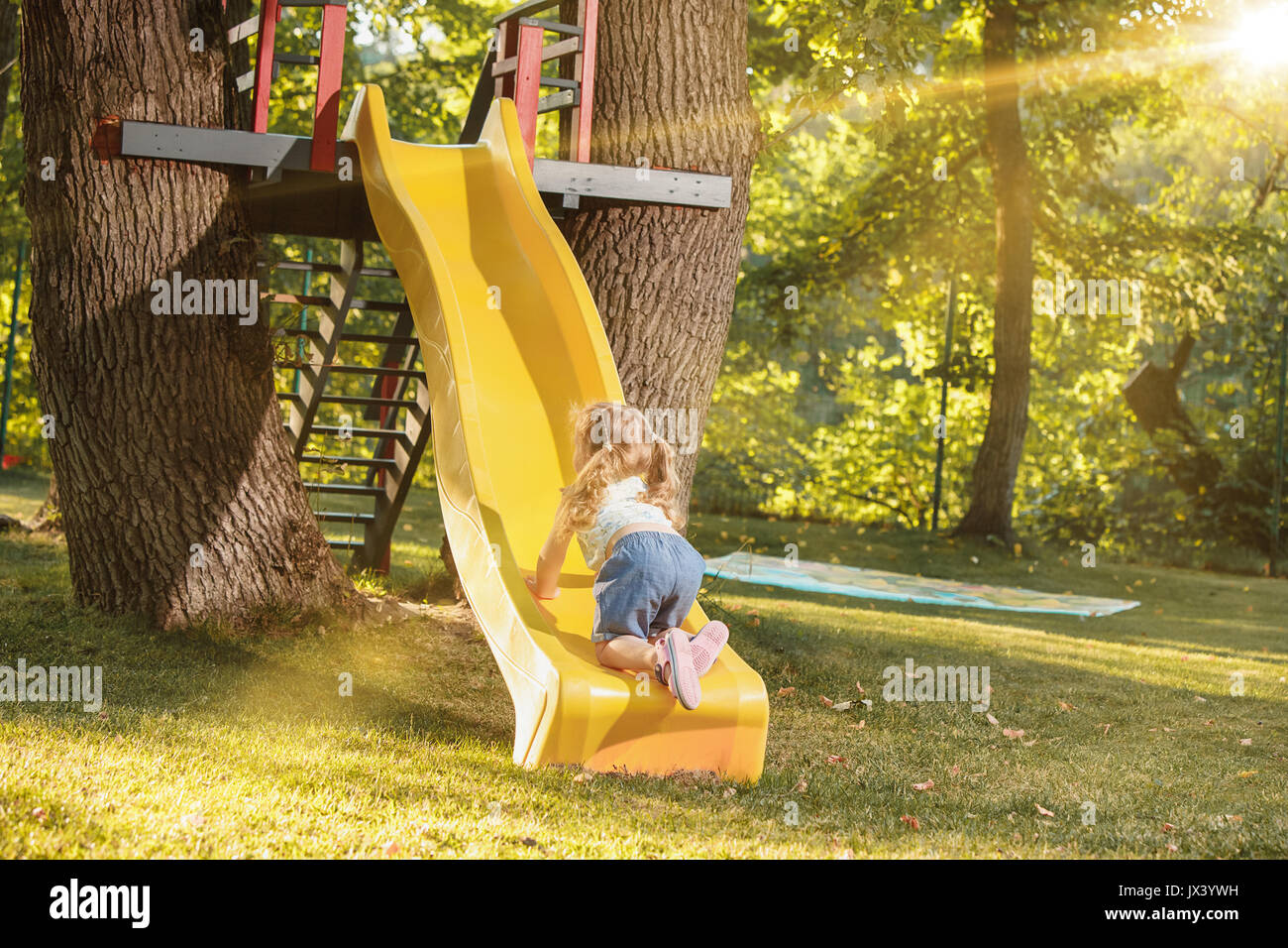 Happy little girl rolling down the hill on the playground Stock Photo ...