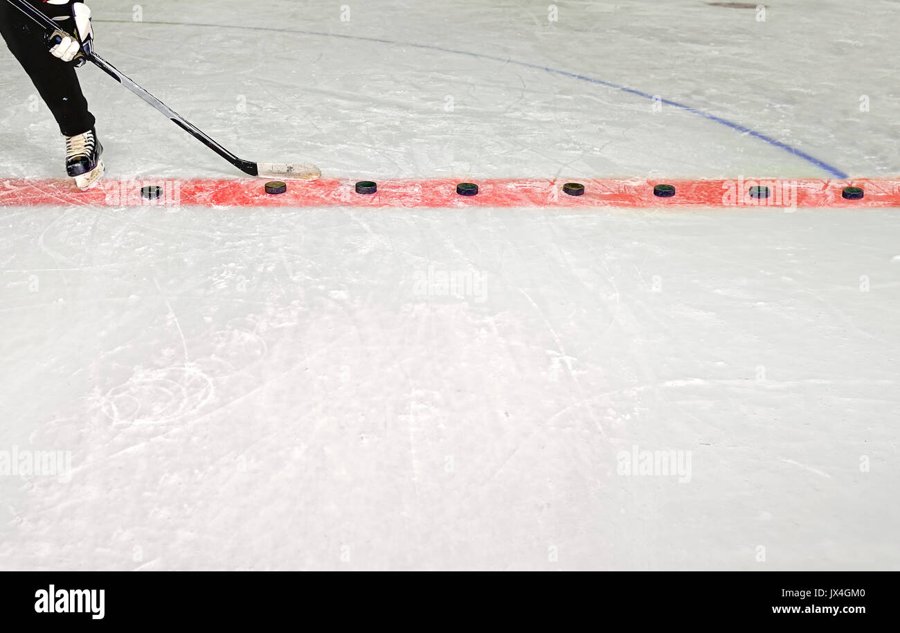 Young Hockey Player Practices Shooting Pucks with stick in Hockey Rink