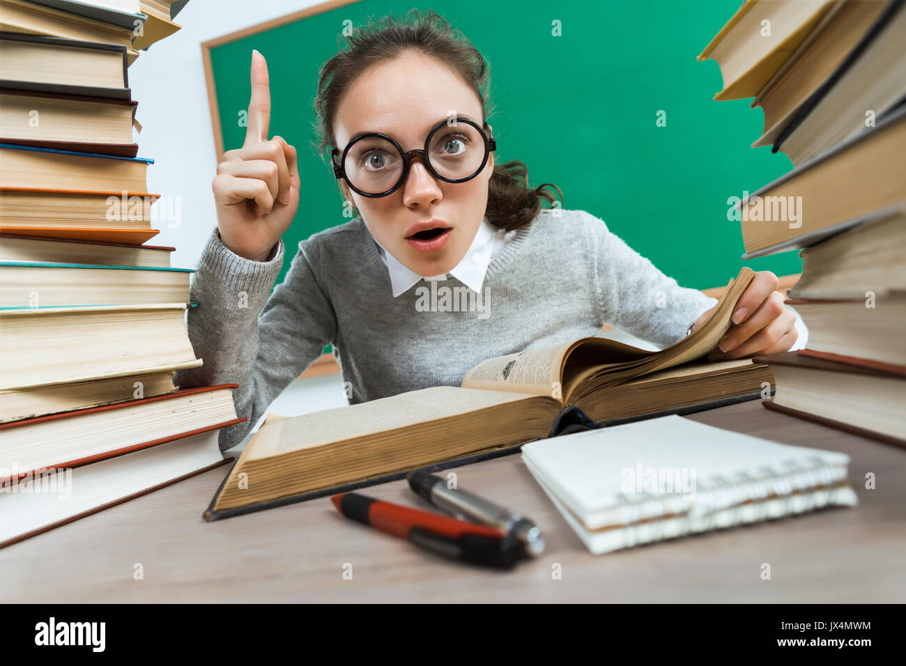 Did you know that?! Curious student reads a books. Photo of astonished young girl wearing glasses pointing finger up. Education concept Stock Photo