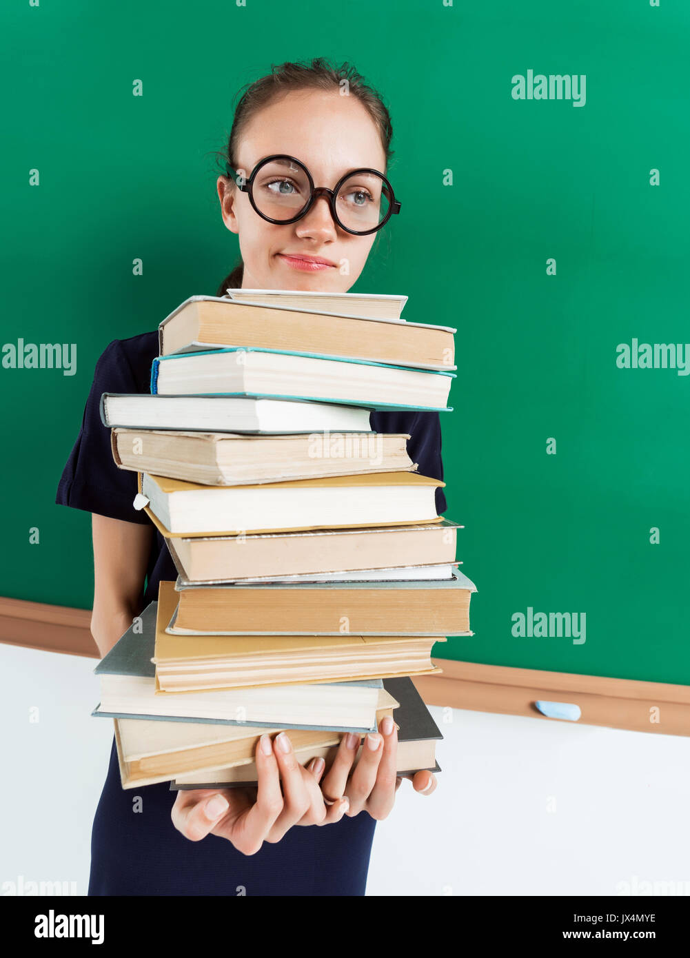 Unhappy student with stack of books near blackboard, education concept. Back to school!! Stock Photo
