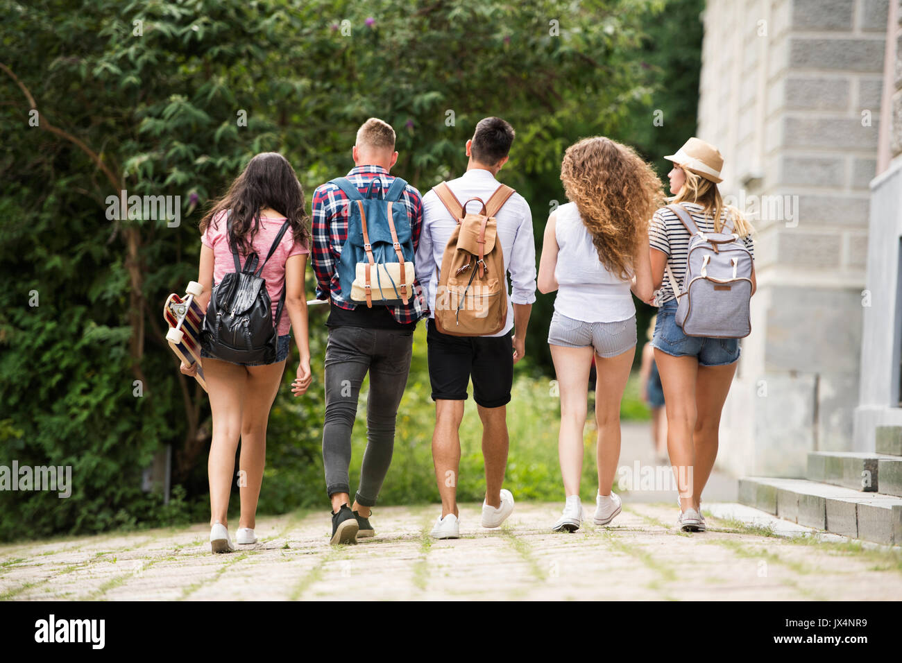 Group of four attractive teenage students walking from university. Rear view. Stock Photo